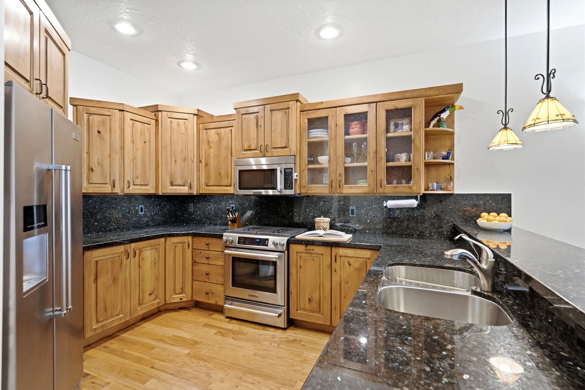 Open-concept kitchen and dining area featuring light wood cabinetry, granite, stainless steel appliances, and wood flooring
