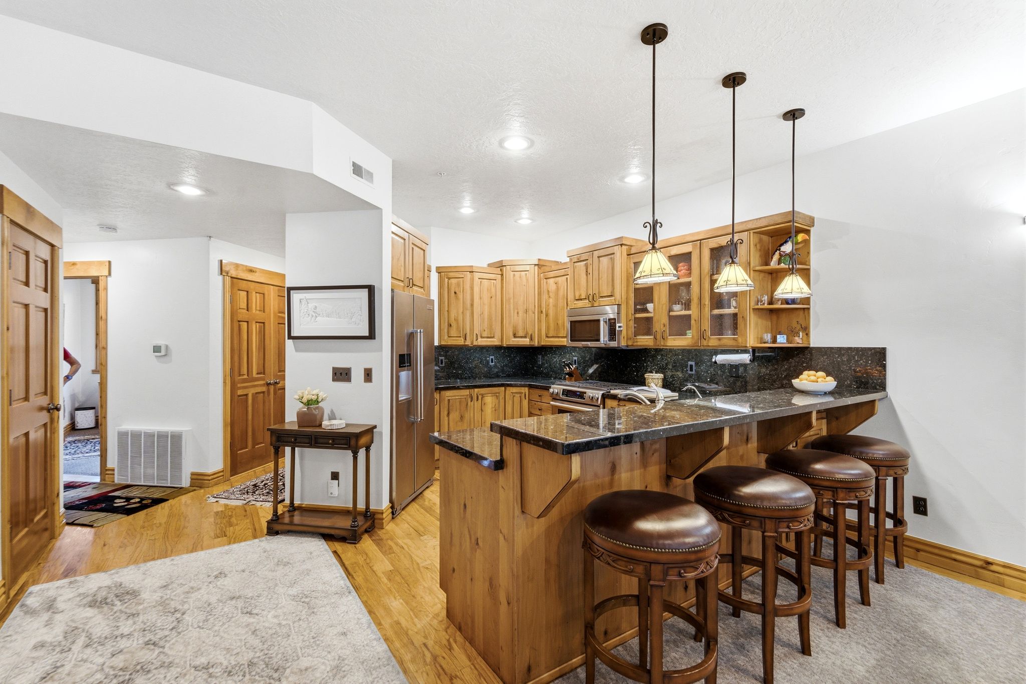 Open-concept kitchen and dining area featuring light wood cabinetry, granite, stainless steel appliances, and wood flooring