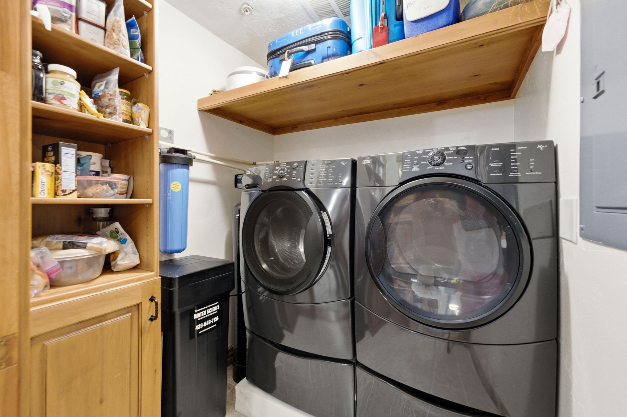 Dedicated laundry area featuring front-loading washer and dryer, built-in shelving, wood-finish cabinetry, and a water filtration system