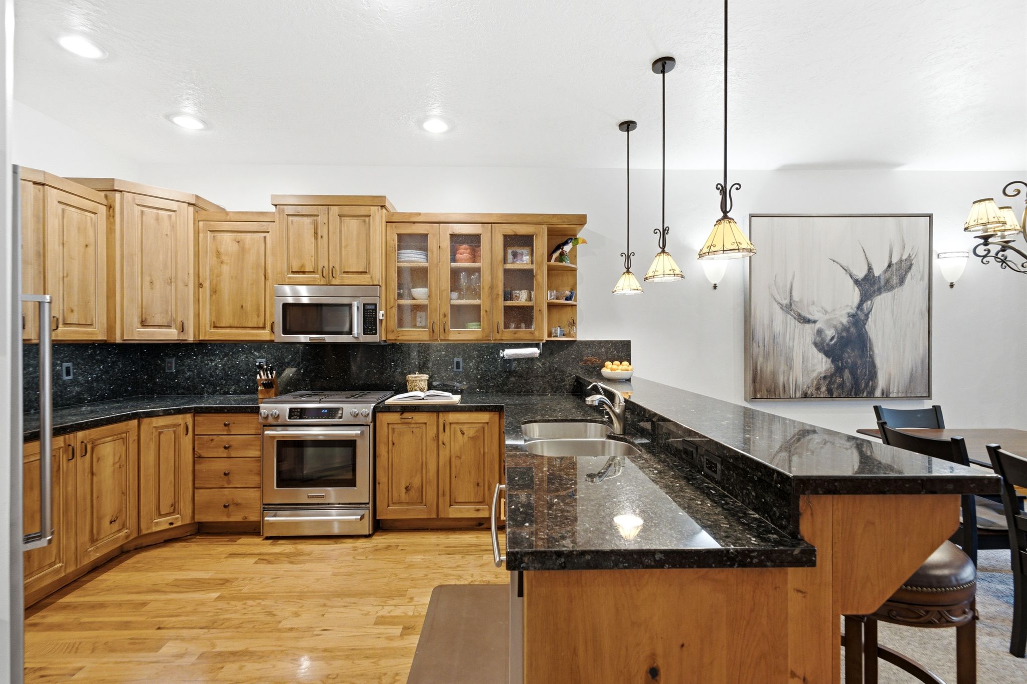 Open-concept kitchen and dining area featuring light wood cabinetry, granite, stainless steel appliances, and wood flooring