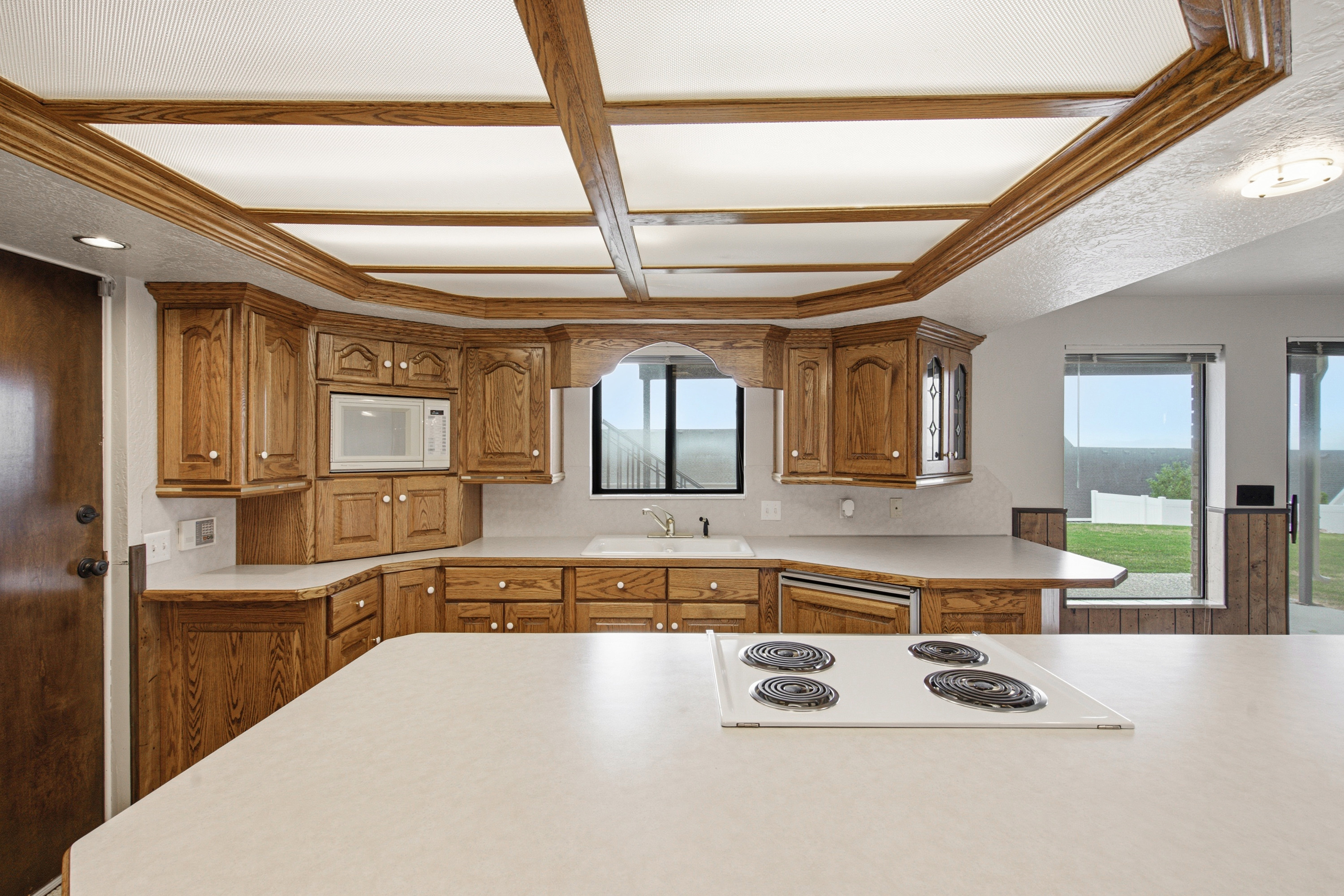 Kitchen featuring wood cabinetry, white countertops, built-in microwave, and a white electric cooktop