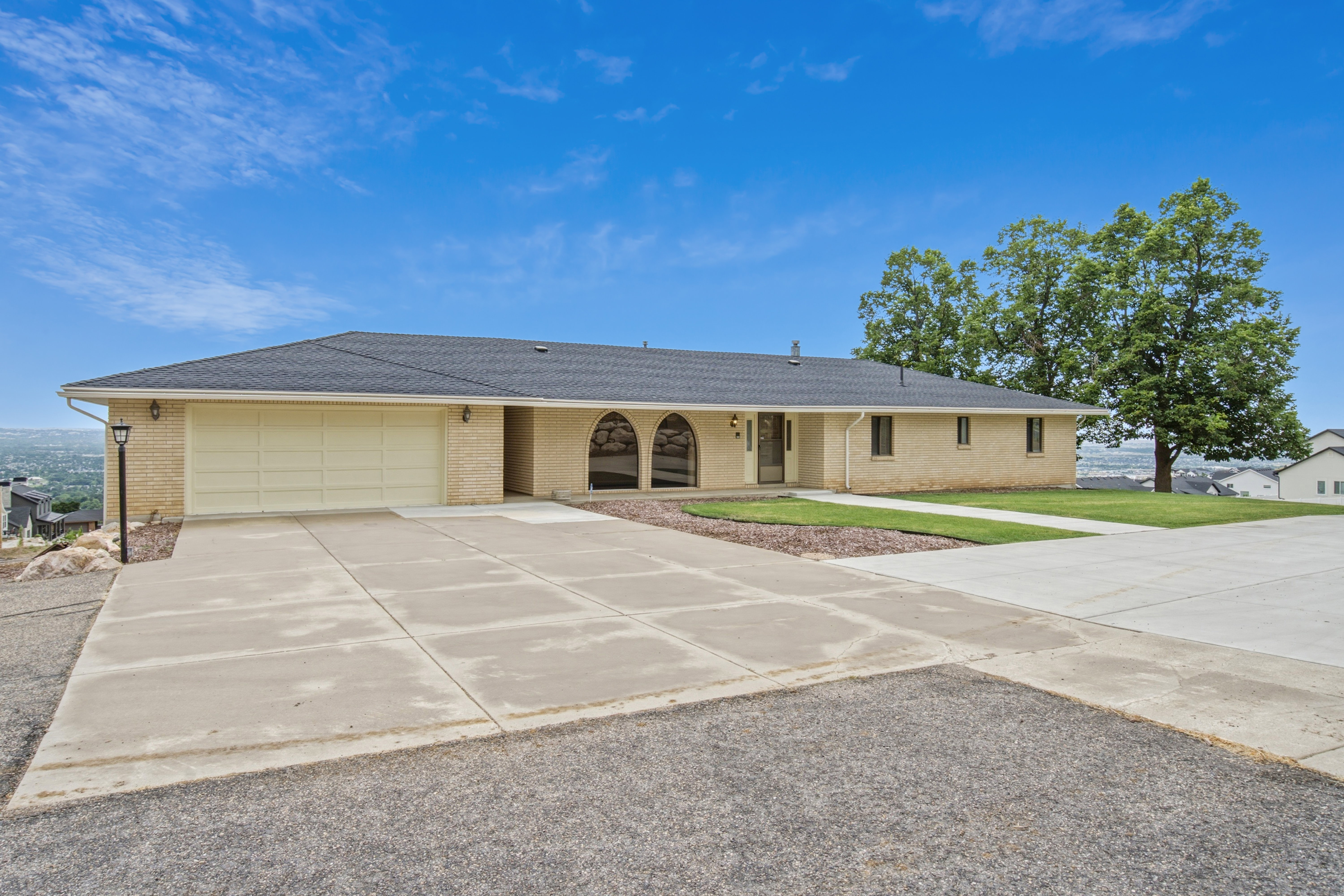 Ranch-style residence featuring a light-colored brick exterior, dark shingle roof, and a two-car garage