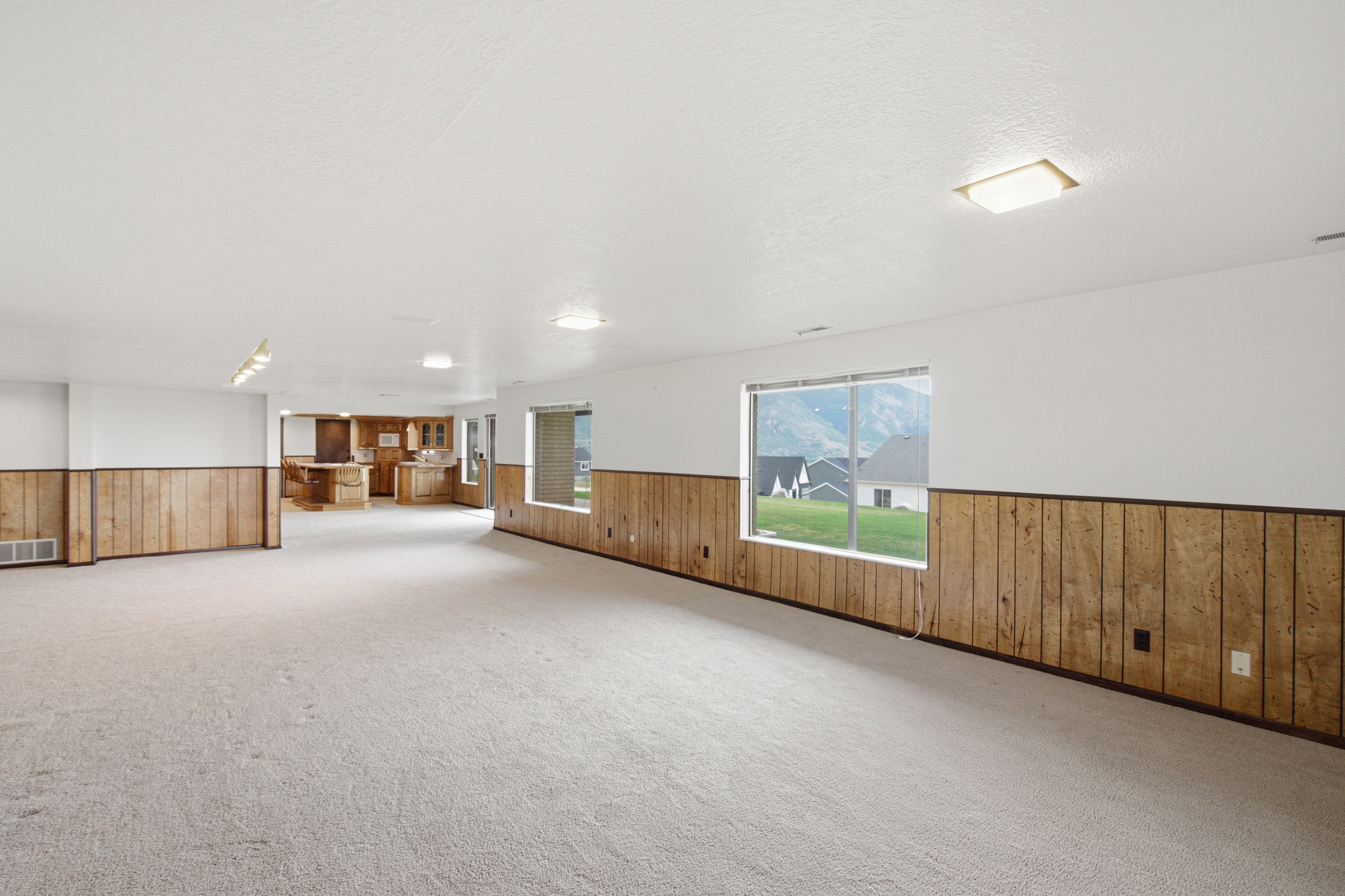 Spacious room featuring light-colored carpeting, white walls, and wood paneling