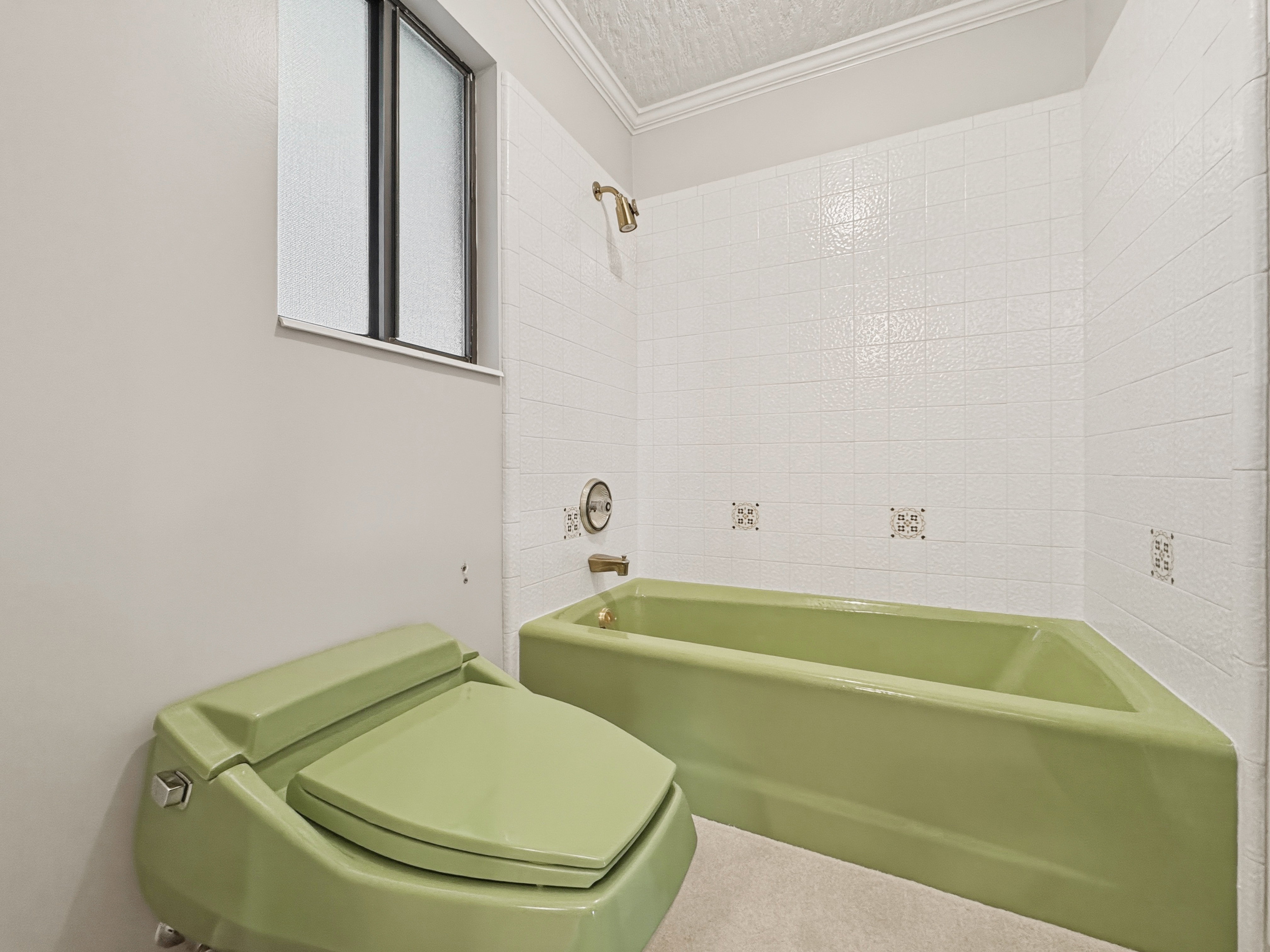 Bathroom featuring a green bathtub and toilet, white tiled walls with decorative accents, an opaque window, and a shower fixture