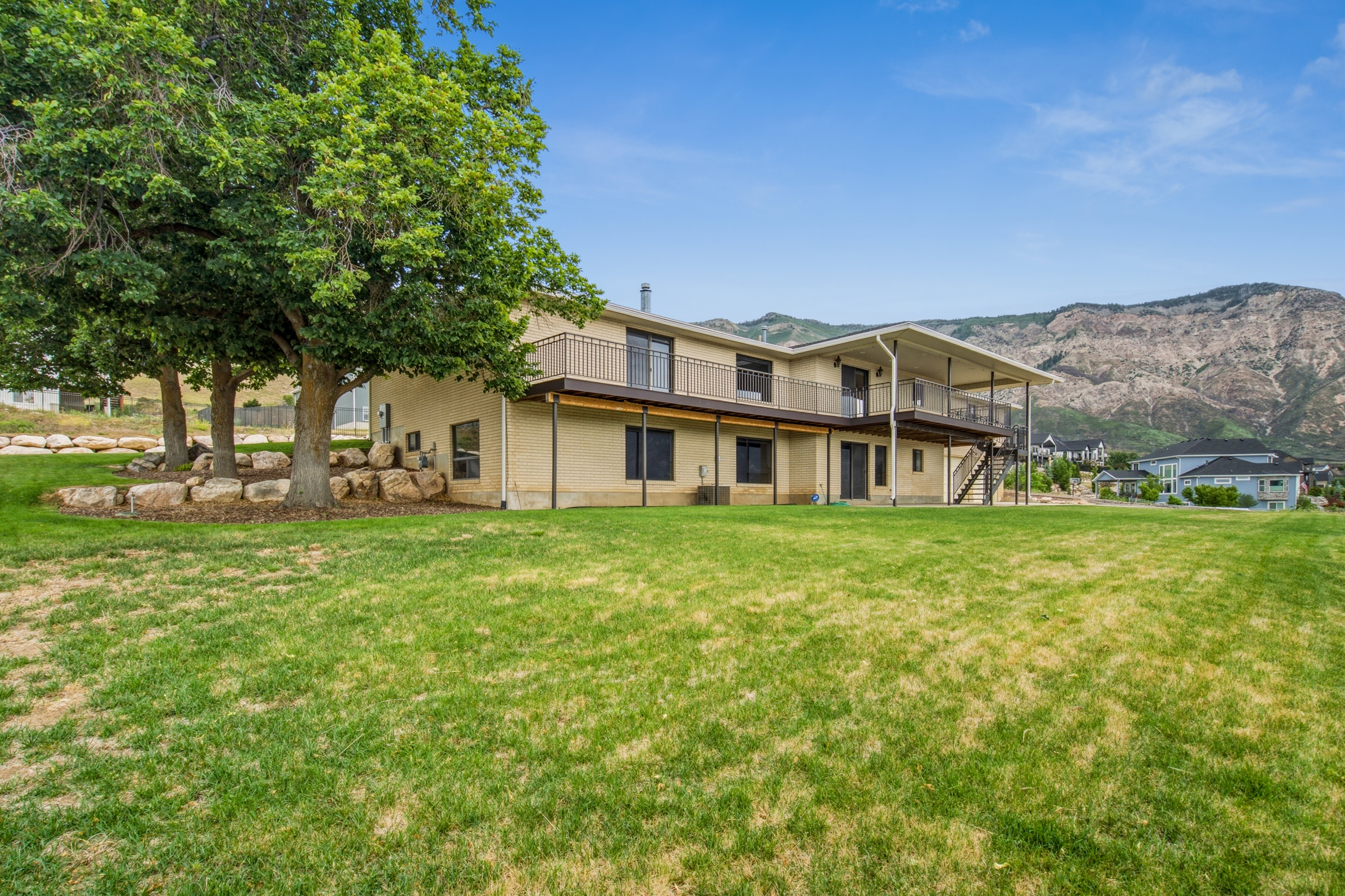 Expansive green lawn with mature trees and a rock landscaping feature