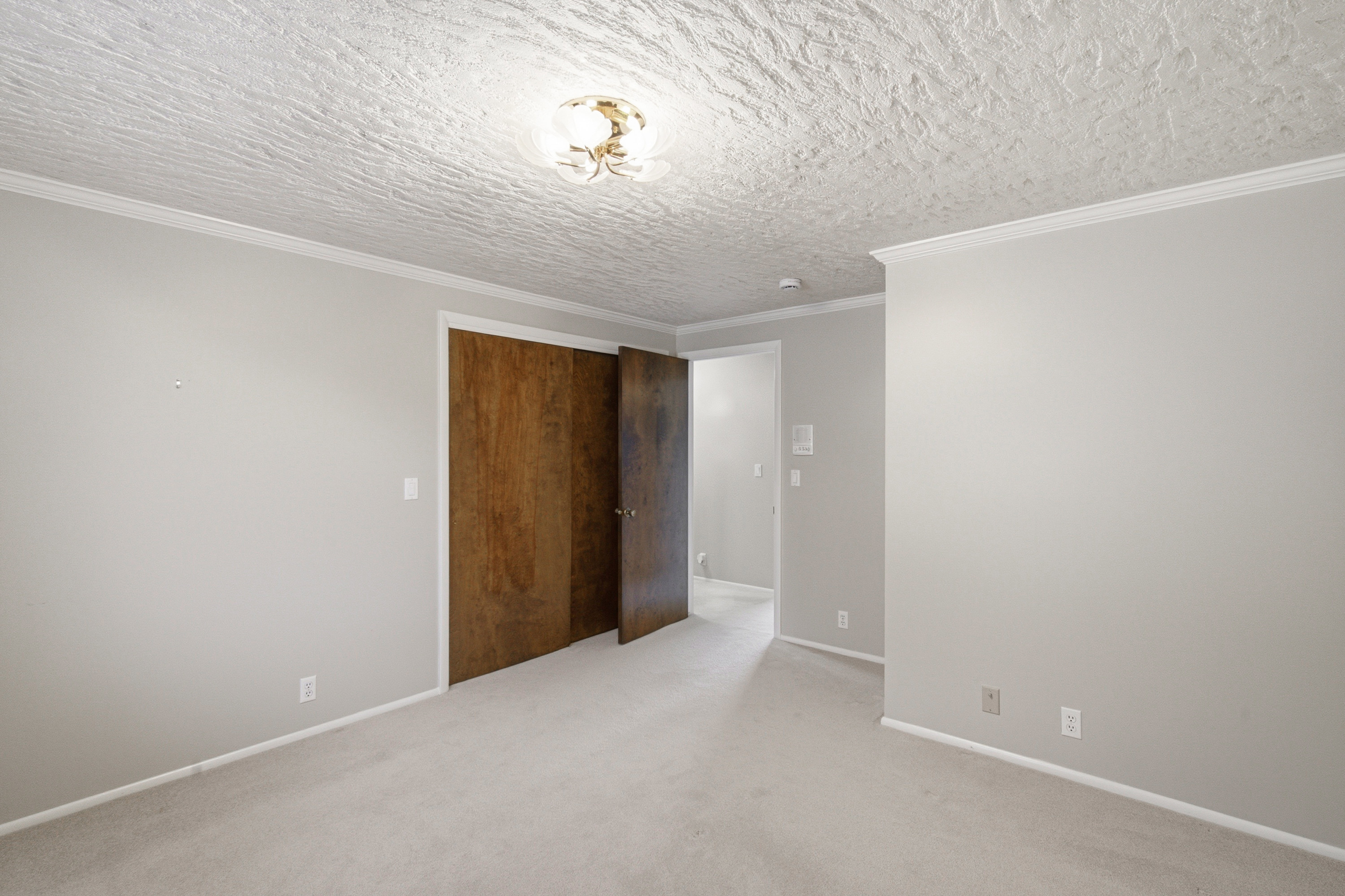 Carpeted room with a textured ceiling, crown molding, and light gray painted walls