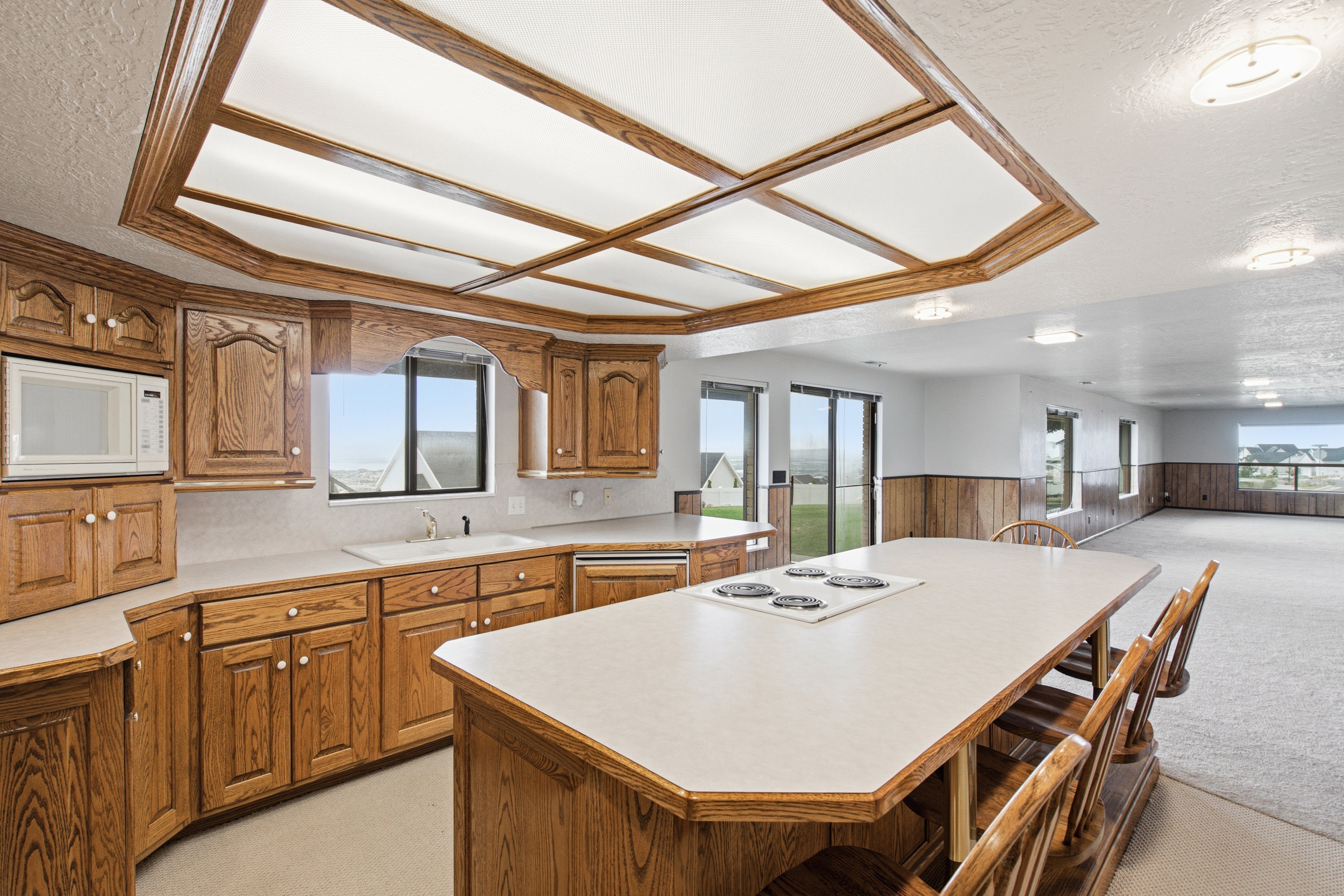Kitchen featuring wood cabinetry, integrated microwave, white countertops, and a central island with a built-in cooktop and seating