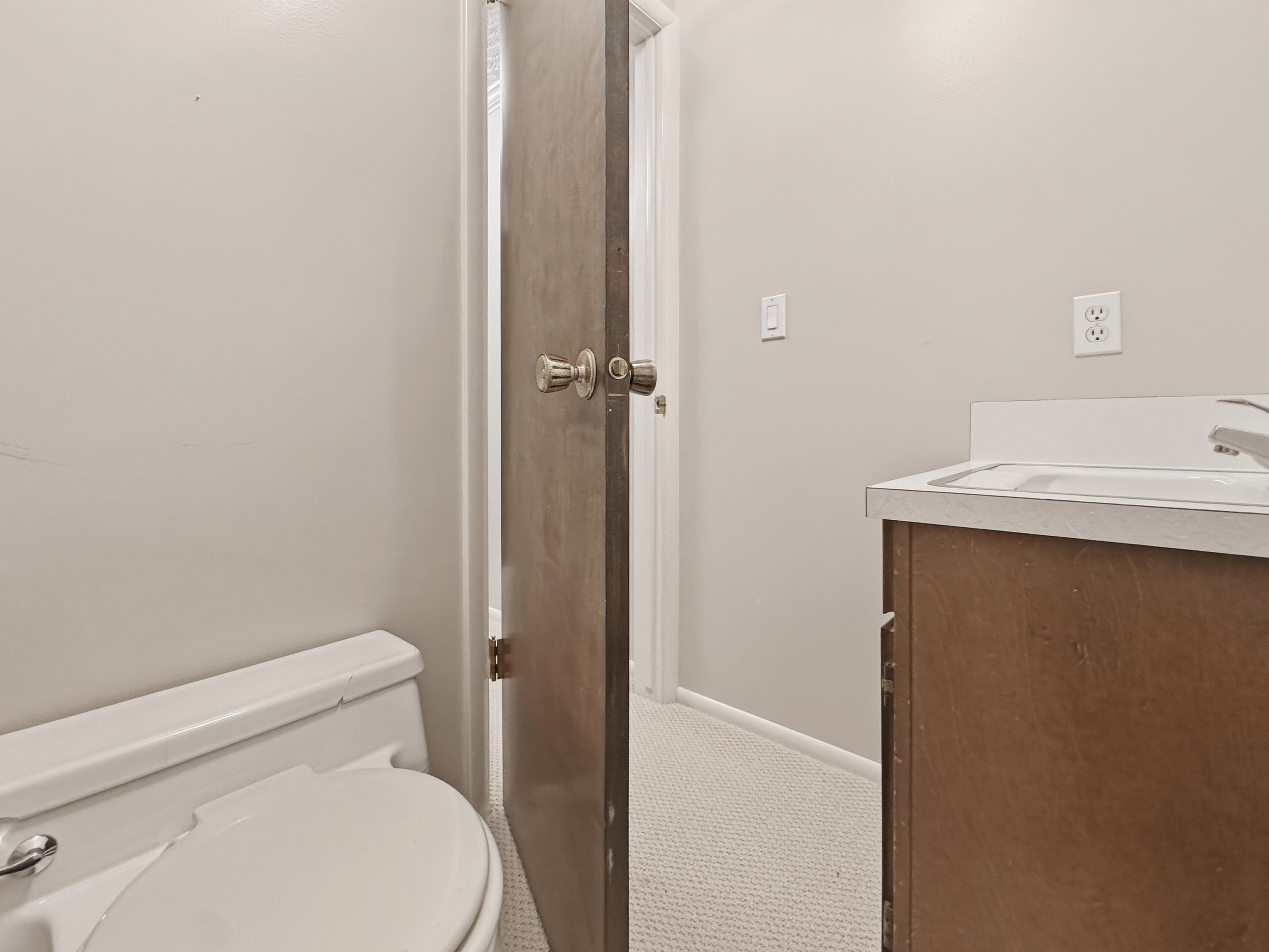 Bathroom featuring a white toilet, light-colored walls, and a vanity with a white countertop and dark wood-finish cabinetry
