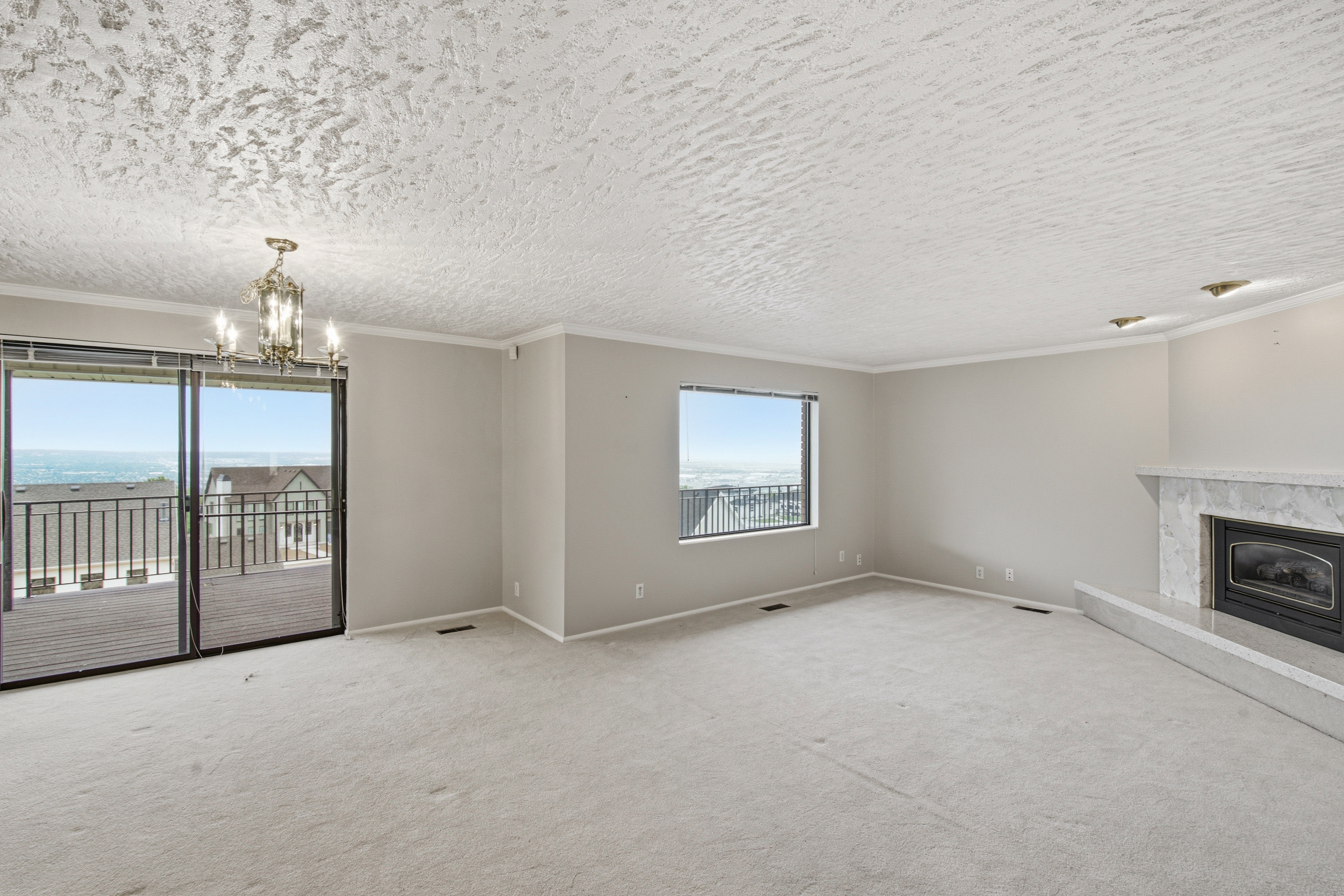 Spacious living area featuring light-colored carpeting, a fireplace with a stone surround and hearth, and crown molding