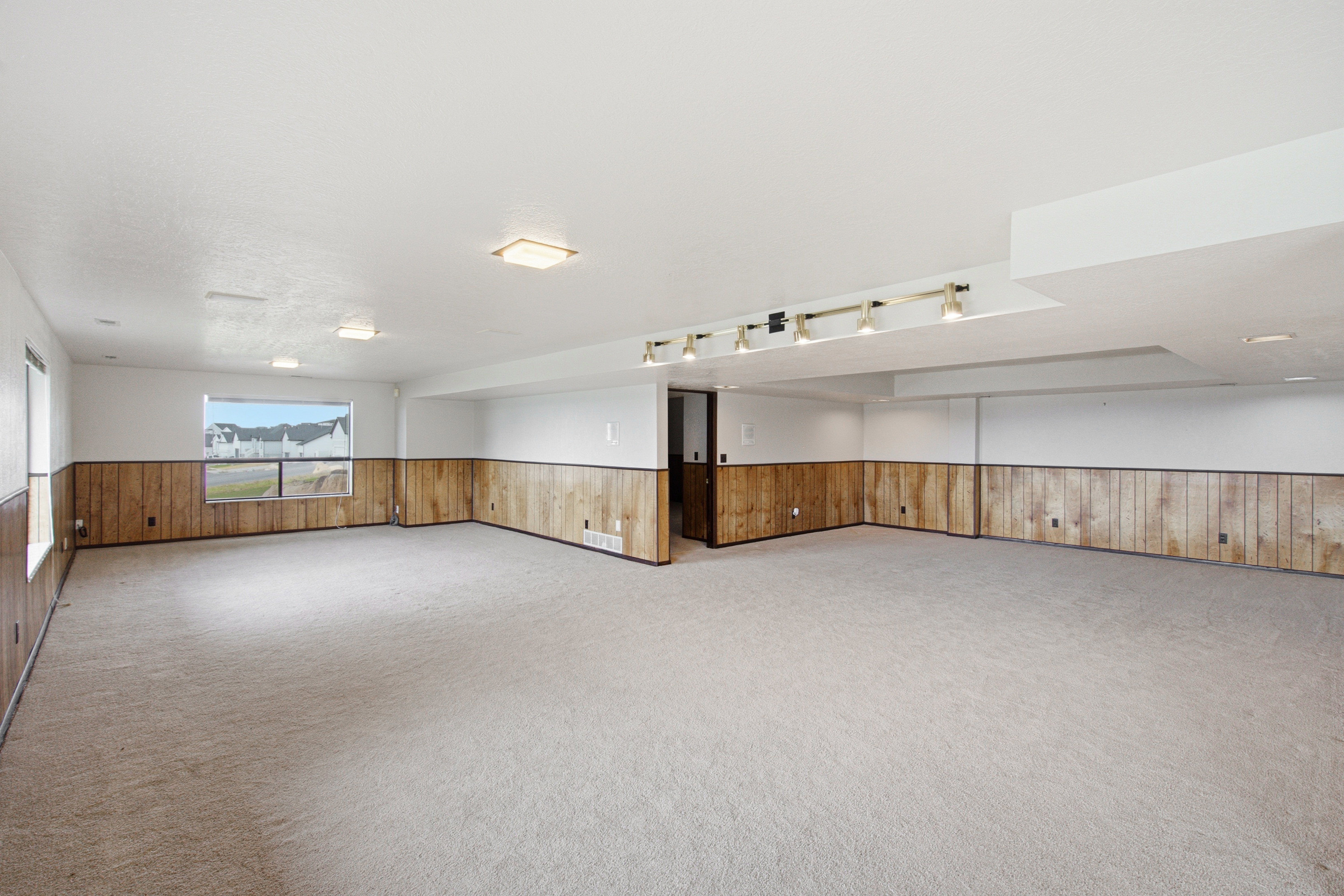Expansive lower level room featuring light-toned carpeting, wood-paneled wainscoting, and white walls