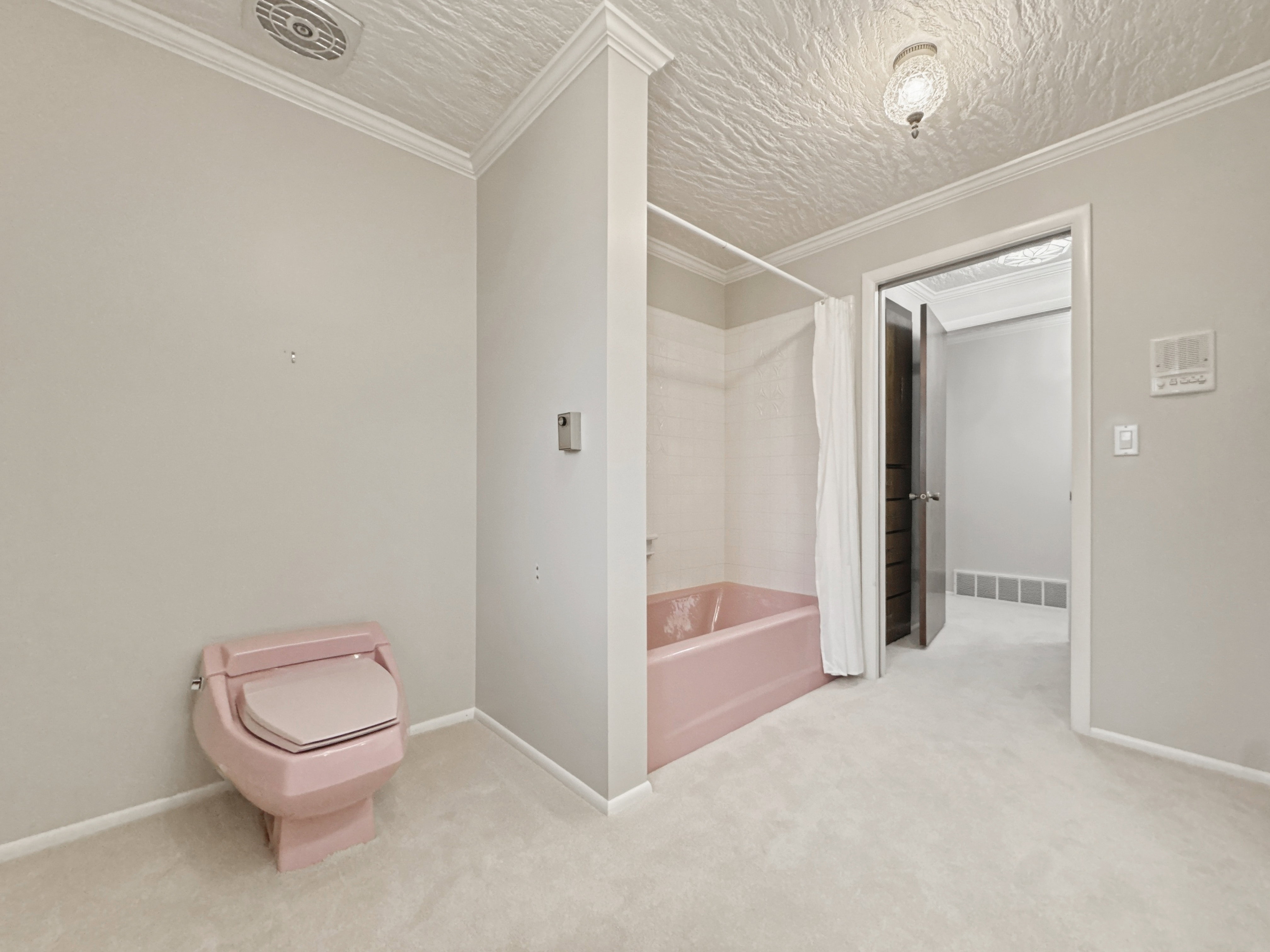 Bathroom featuring a pink toilet, a pink bathtub with a shower curtain, light-colored carpet flooring, crown molding, and a textured ceiling