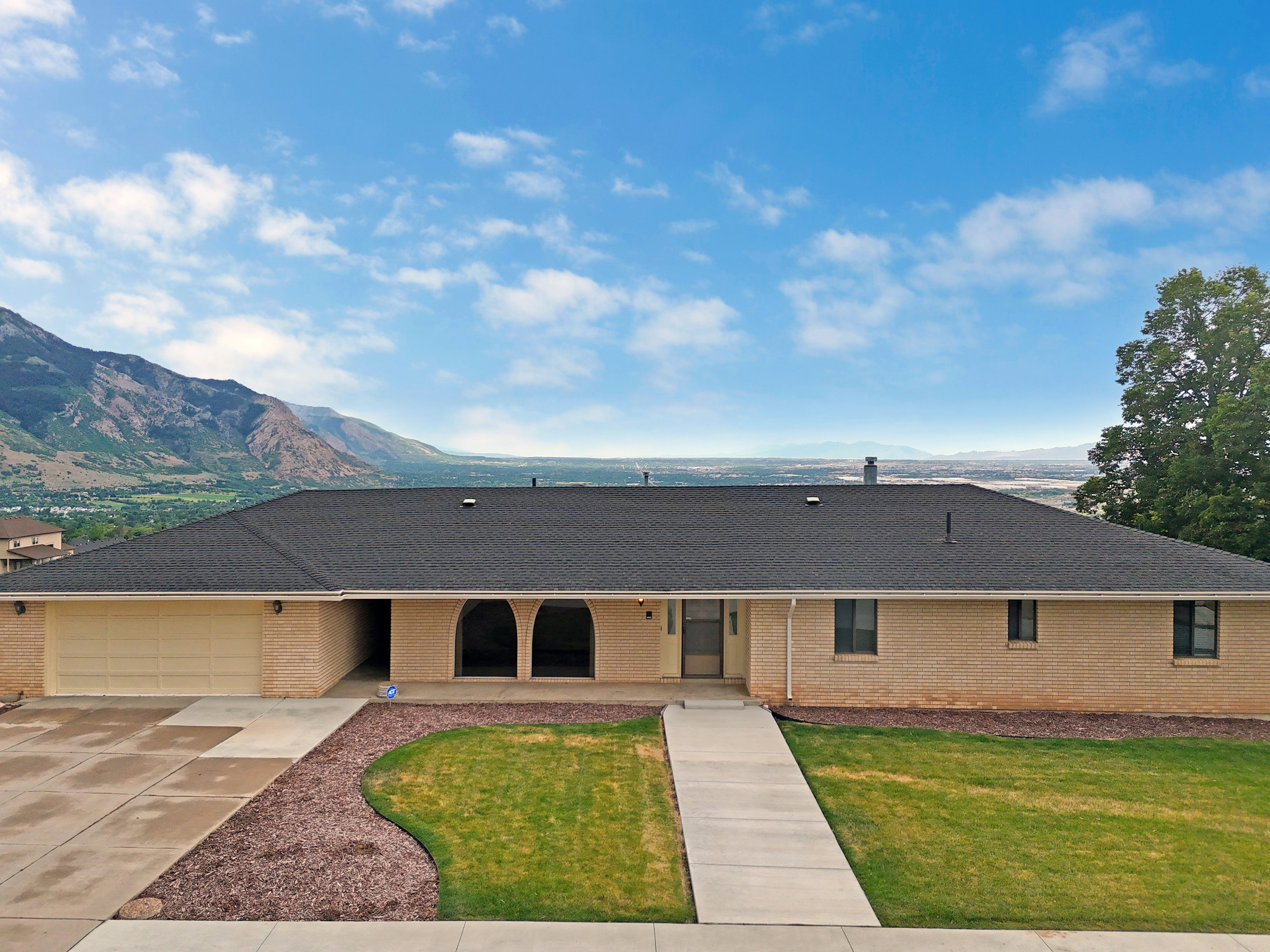 Single-story residence featuring light brick exterior, dark shingle roof, and an attached two-car garage