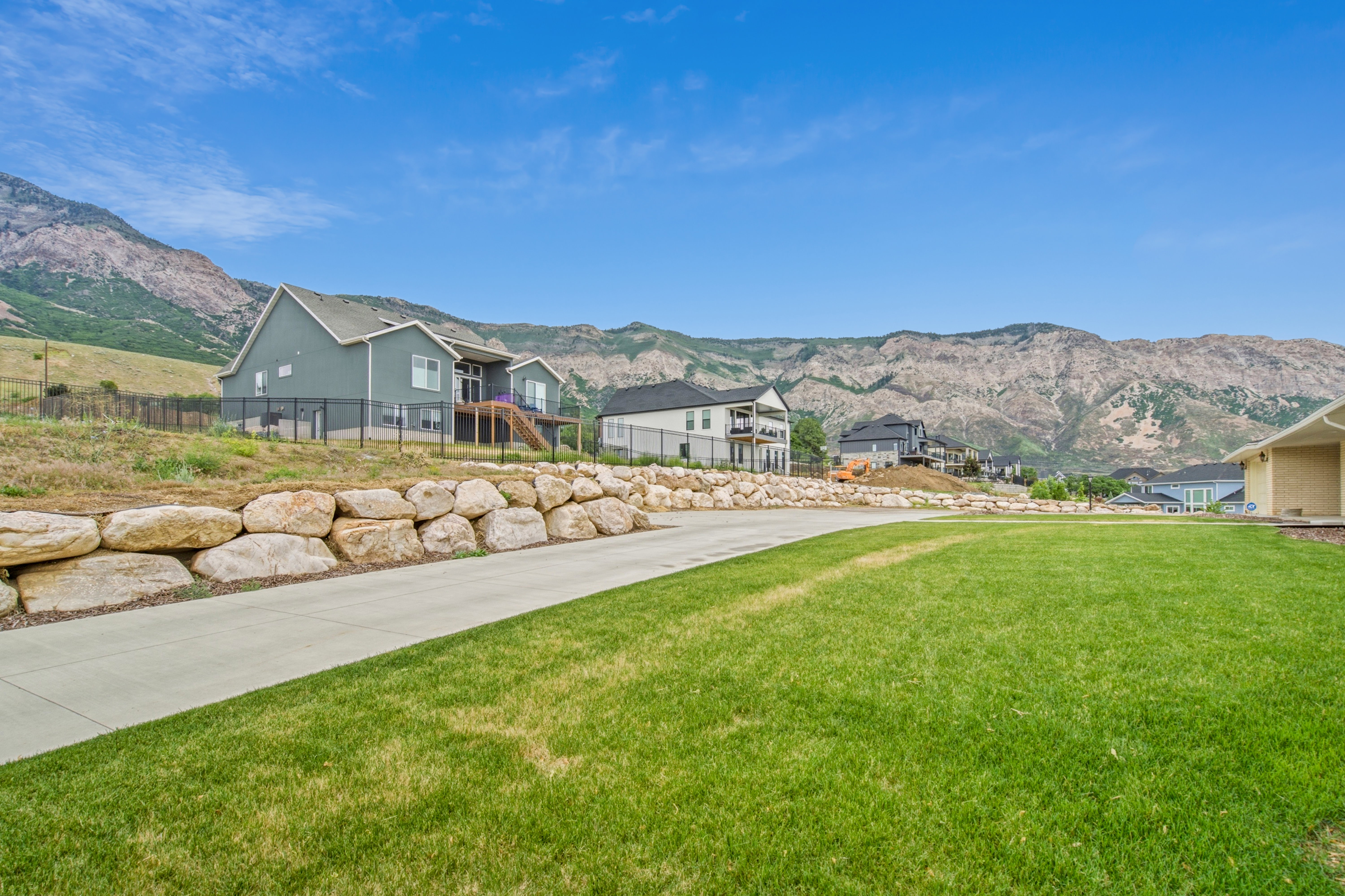 Expansive green lawn with a paved driveway, bordered by a large rock retaining wall
