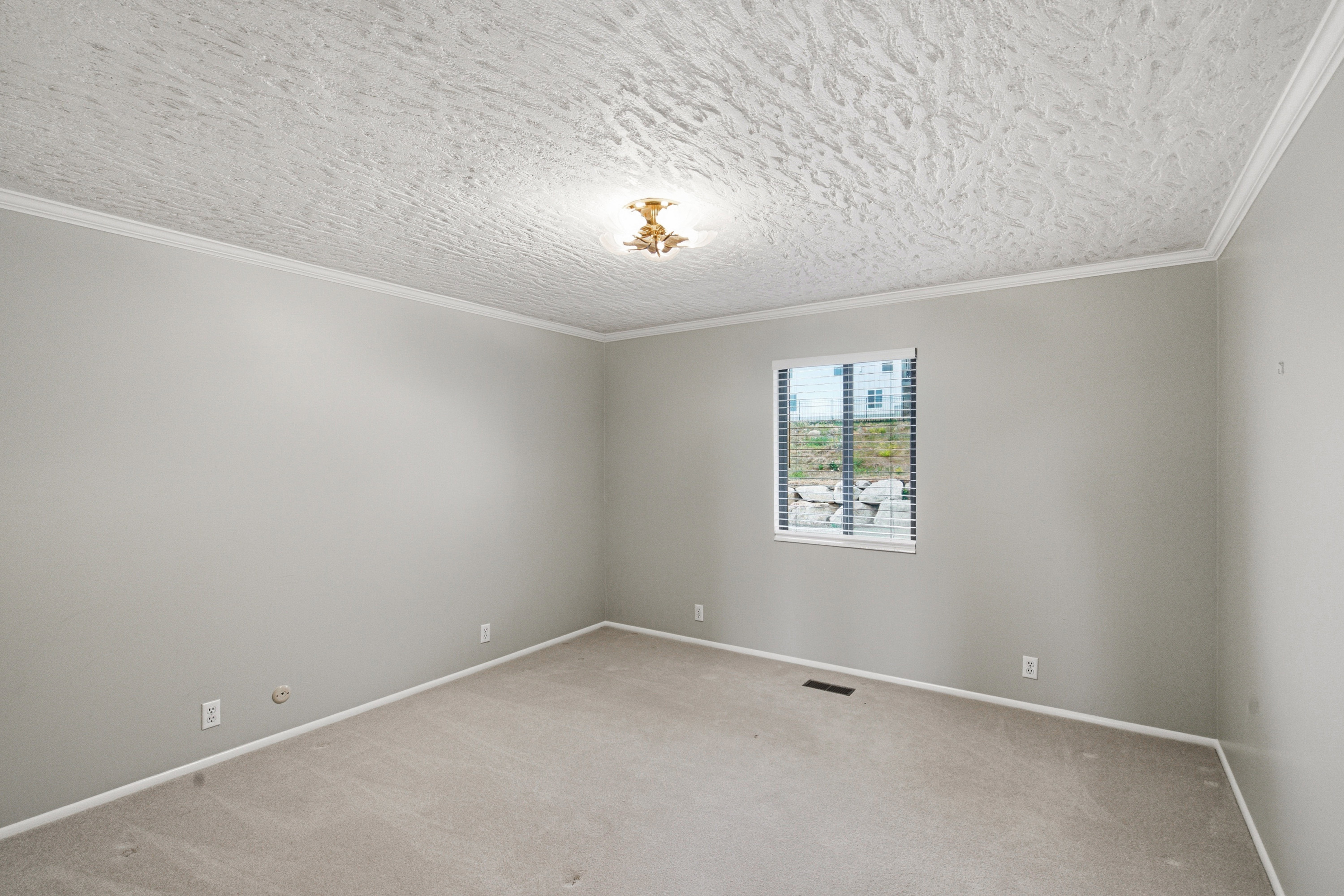 Carpeted interior space with light gray walls, crown molding, a central ceiling light fixture, and a window with horizontal blinds