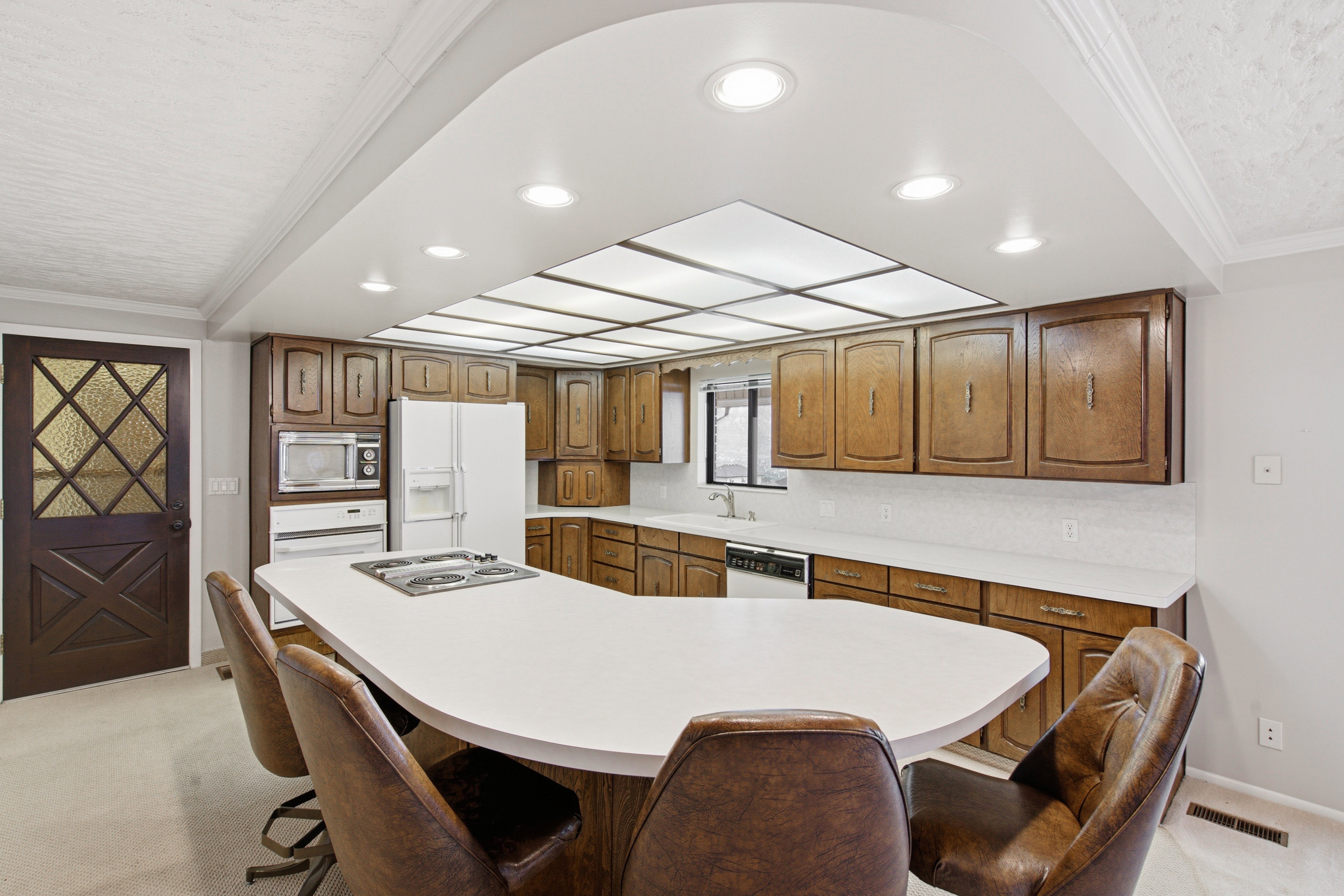 Kitchen featuring wood cabinetry, white countertops, a cooktop island, recessed lighting, and a decorative glass-paneled door