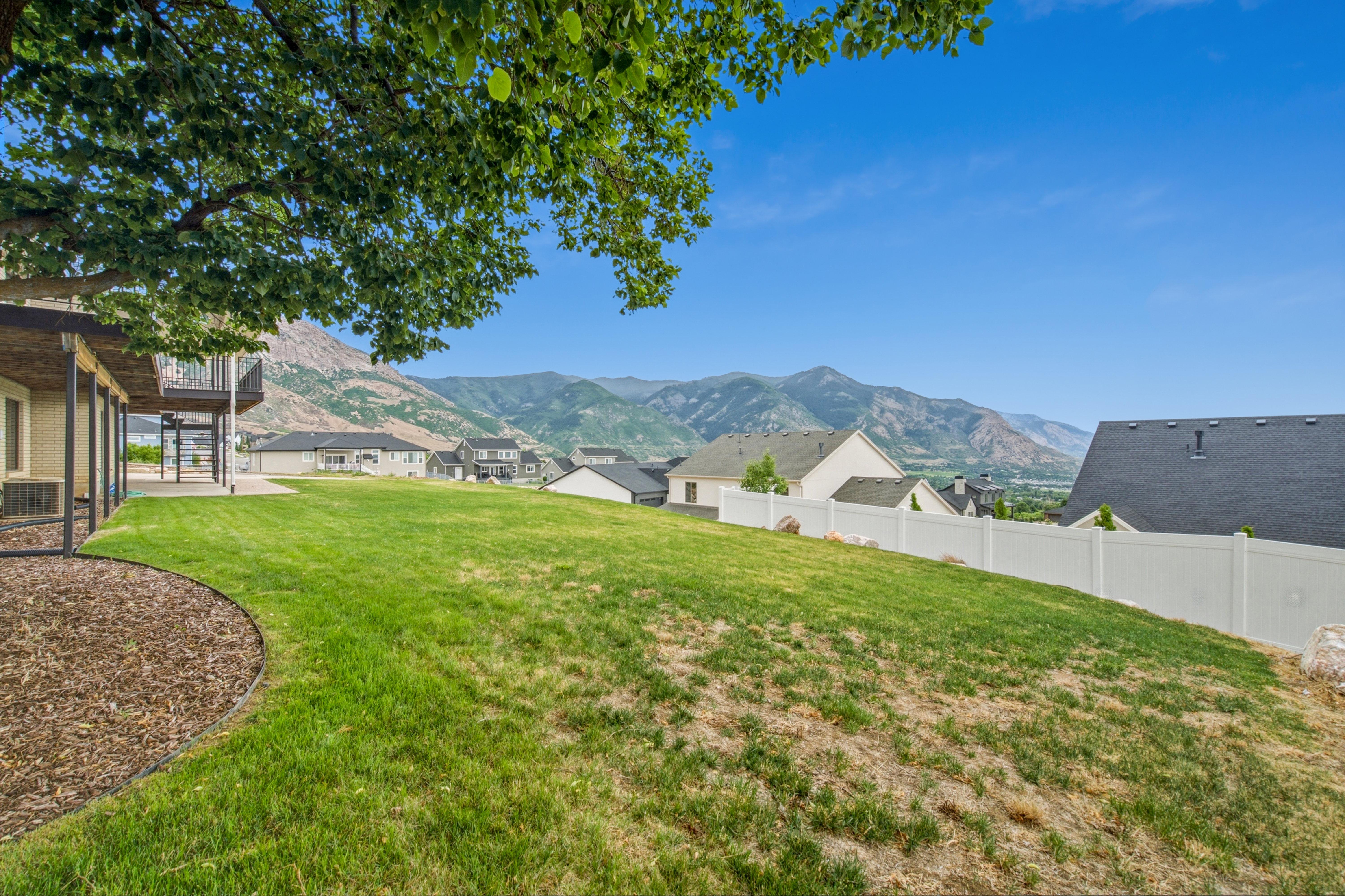 Expansive backyard featuring a large grassy area, a covered patio, and a white privacy fence