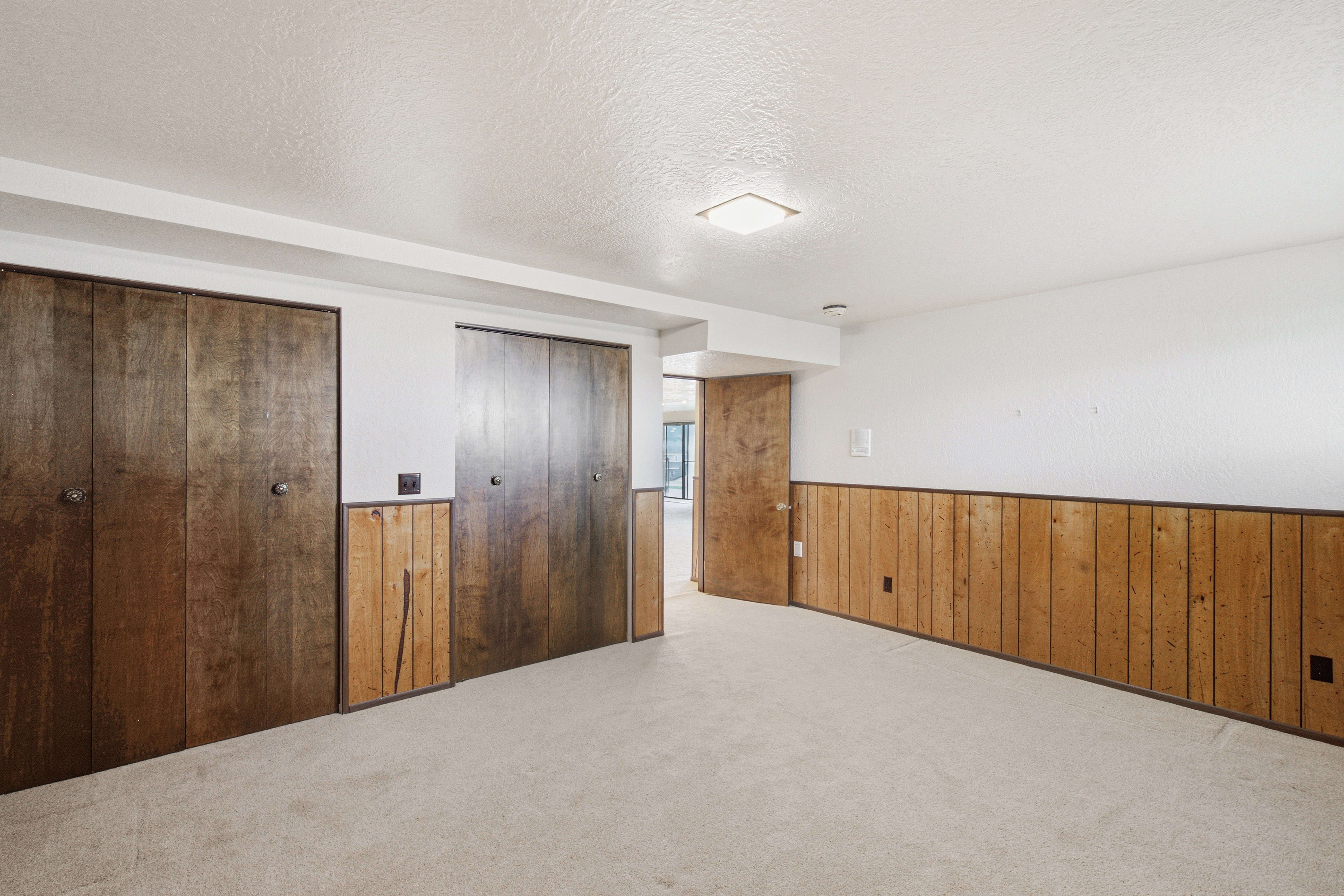 Room featuring light-colored carpeting, white painted walls, and wood paneling on the lower portion of the walls
