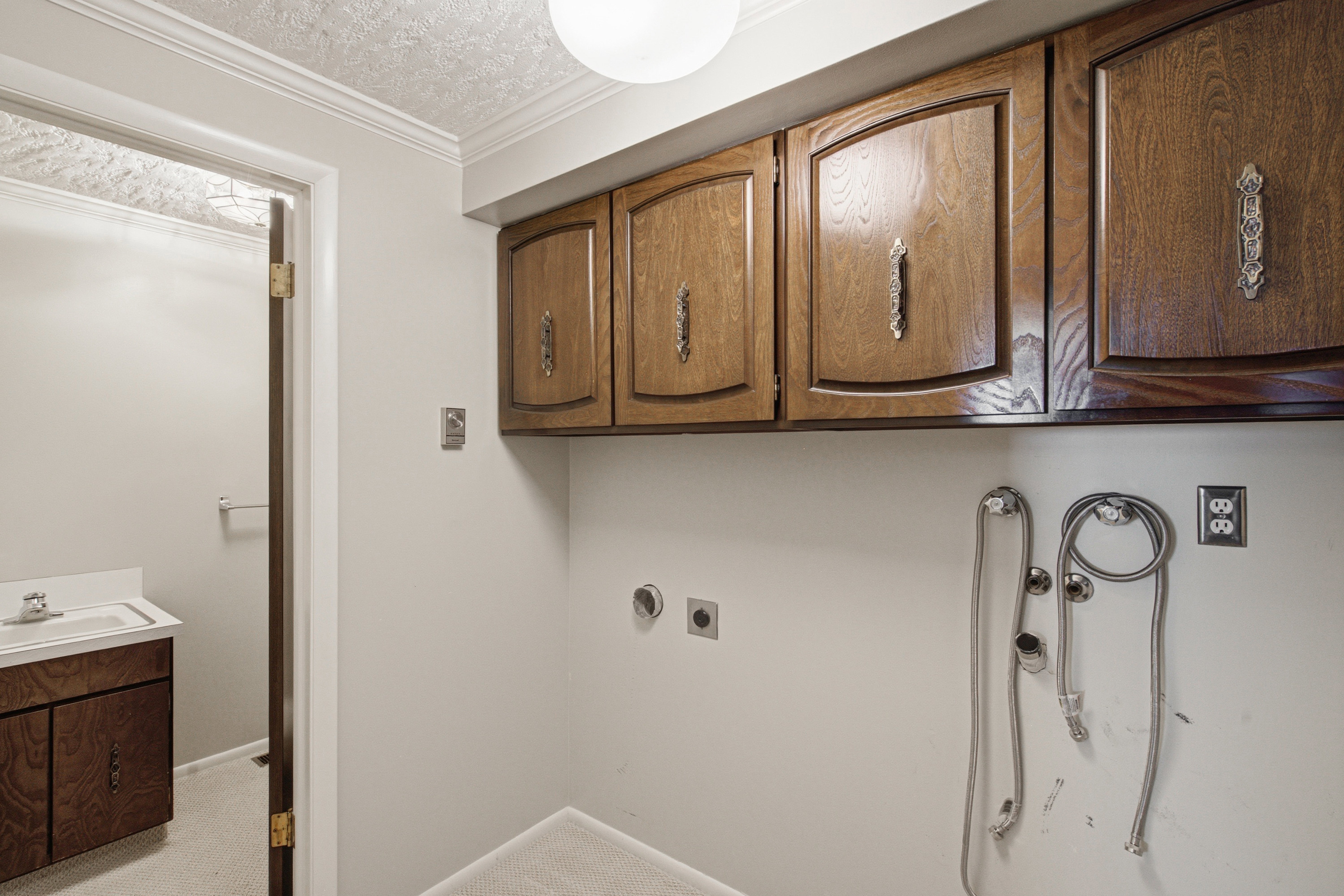 Utility room featuring wood-finish cabinetry with decorative hardware, white walls, and a textured ceiling
