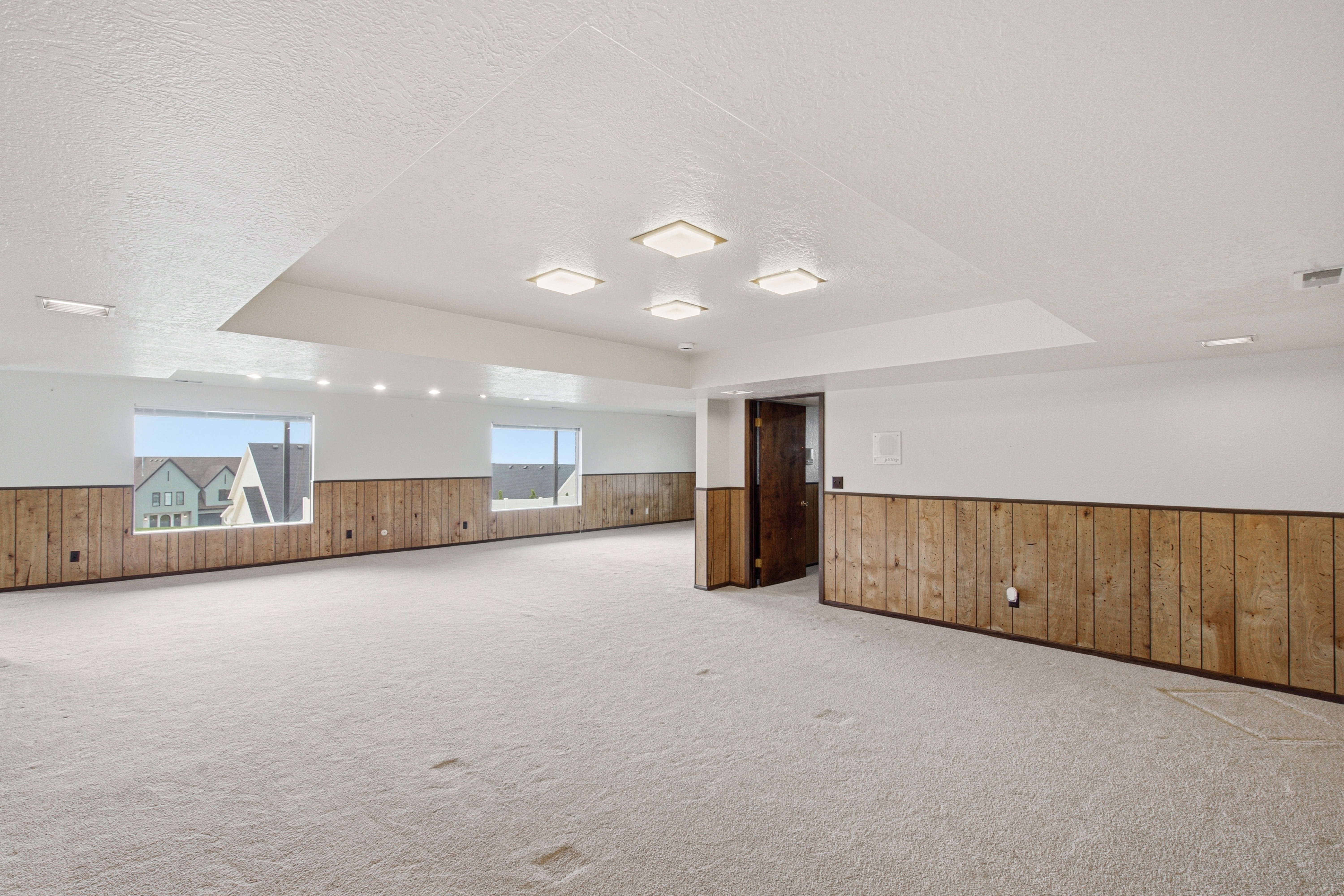 Expansive room featuring light-colored carpeting and wood-paneling accents