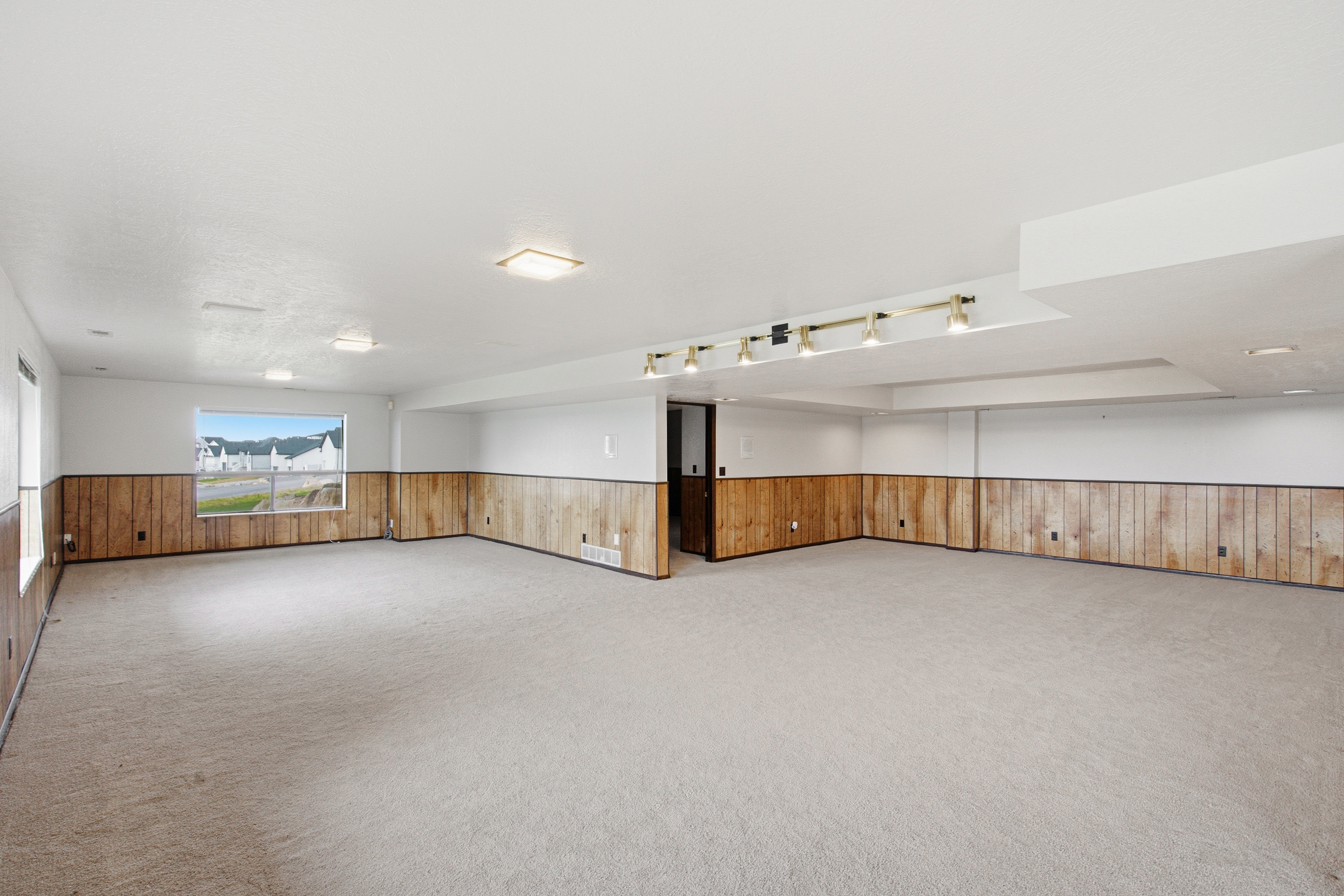 Spacious room featuring light-toned carpet flooring and wood-paneled wainscoting