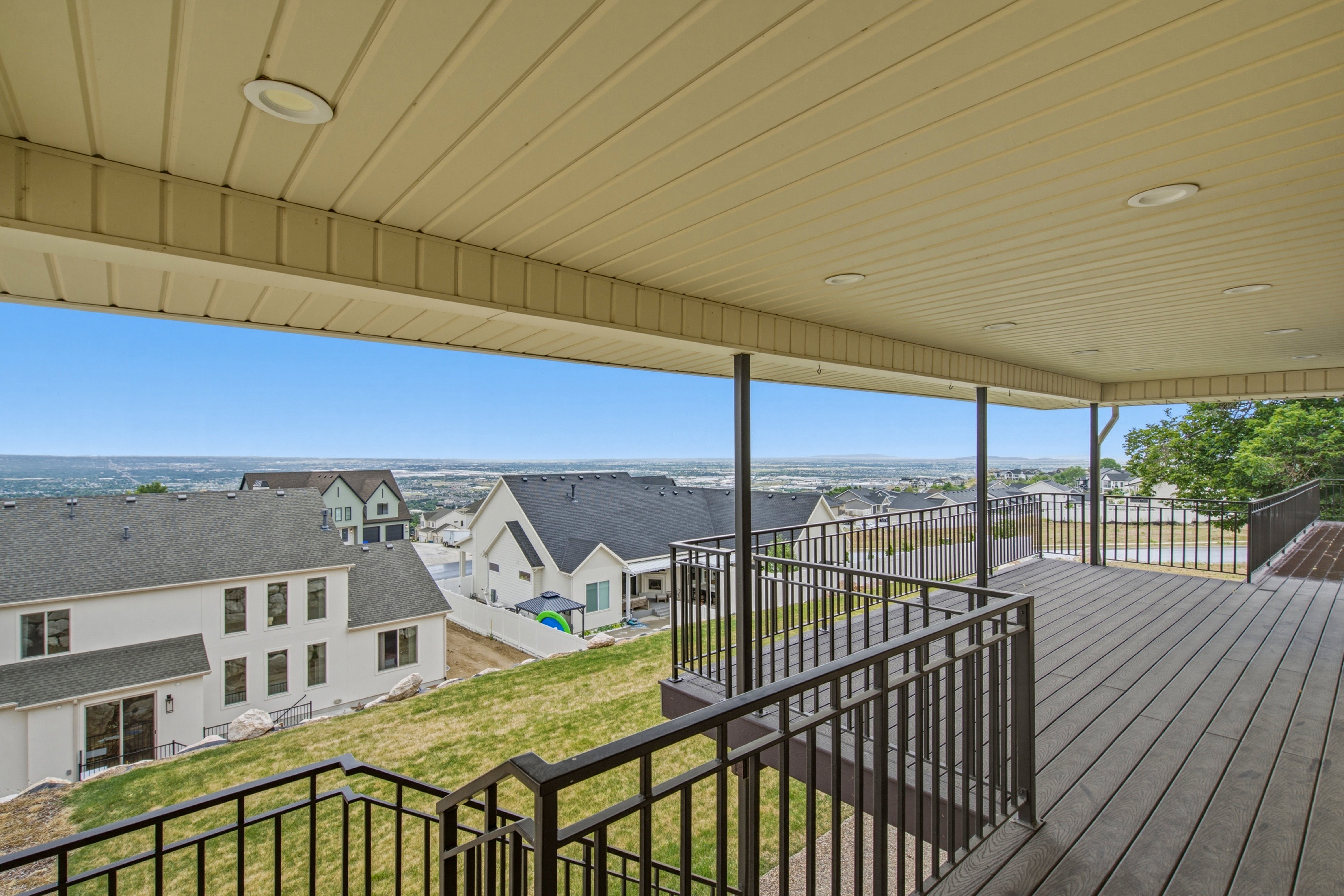 Covered deck featuring composite decking, metal railings, recessed lighting, and a panoramic skyline