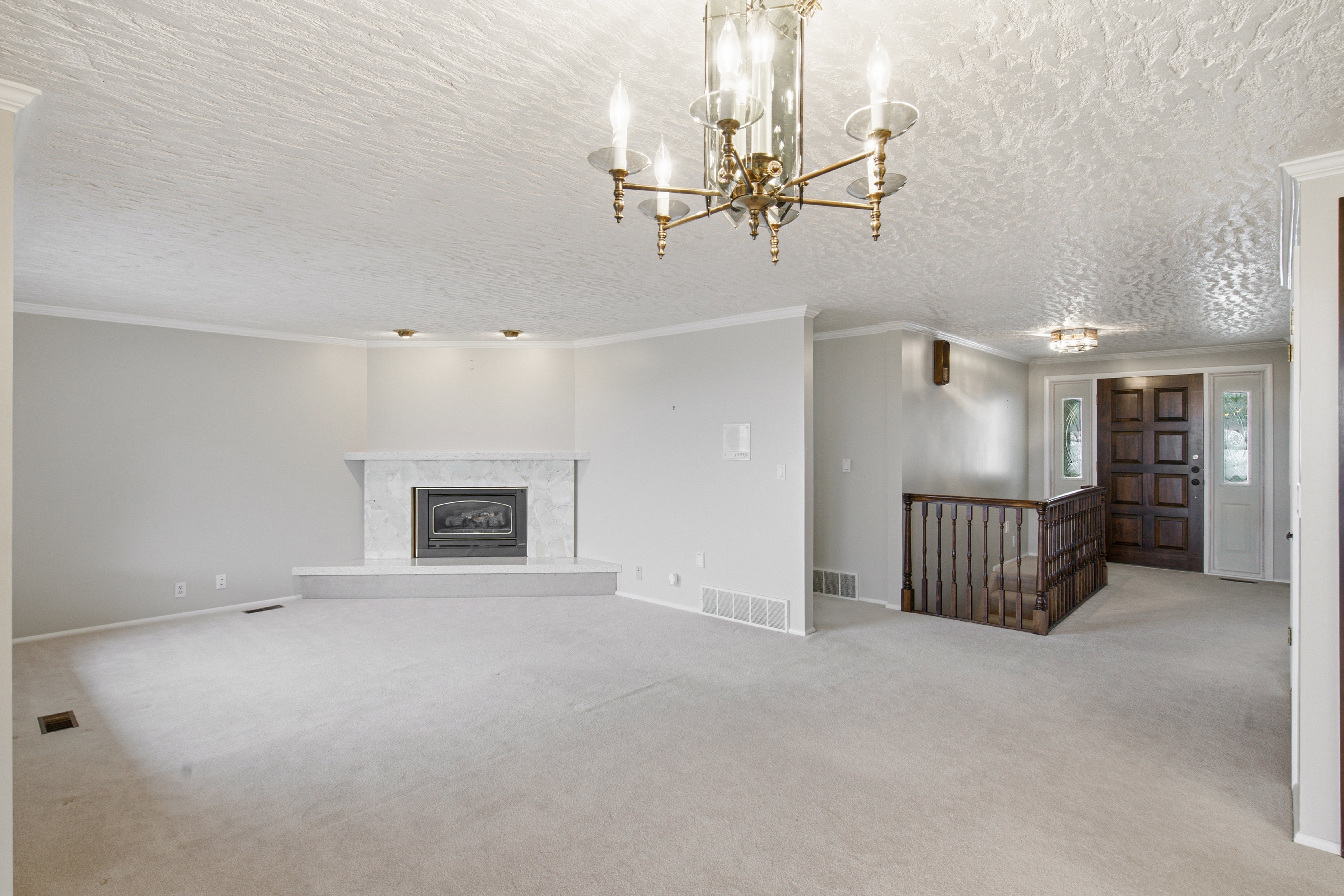 Spacious living area featuring a central fireplace with a stone surround, a prominent brass chandelier, and light-colored carpeting