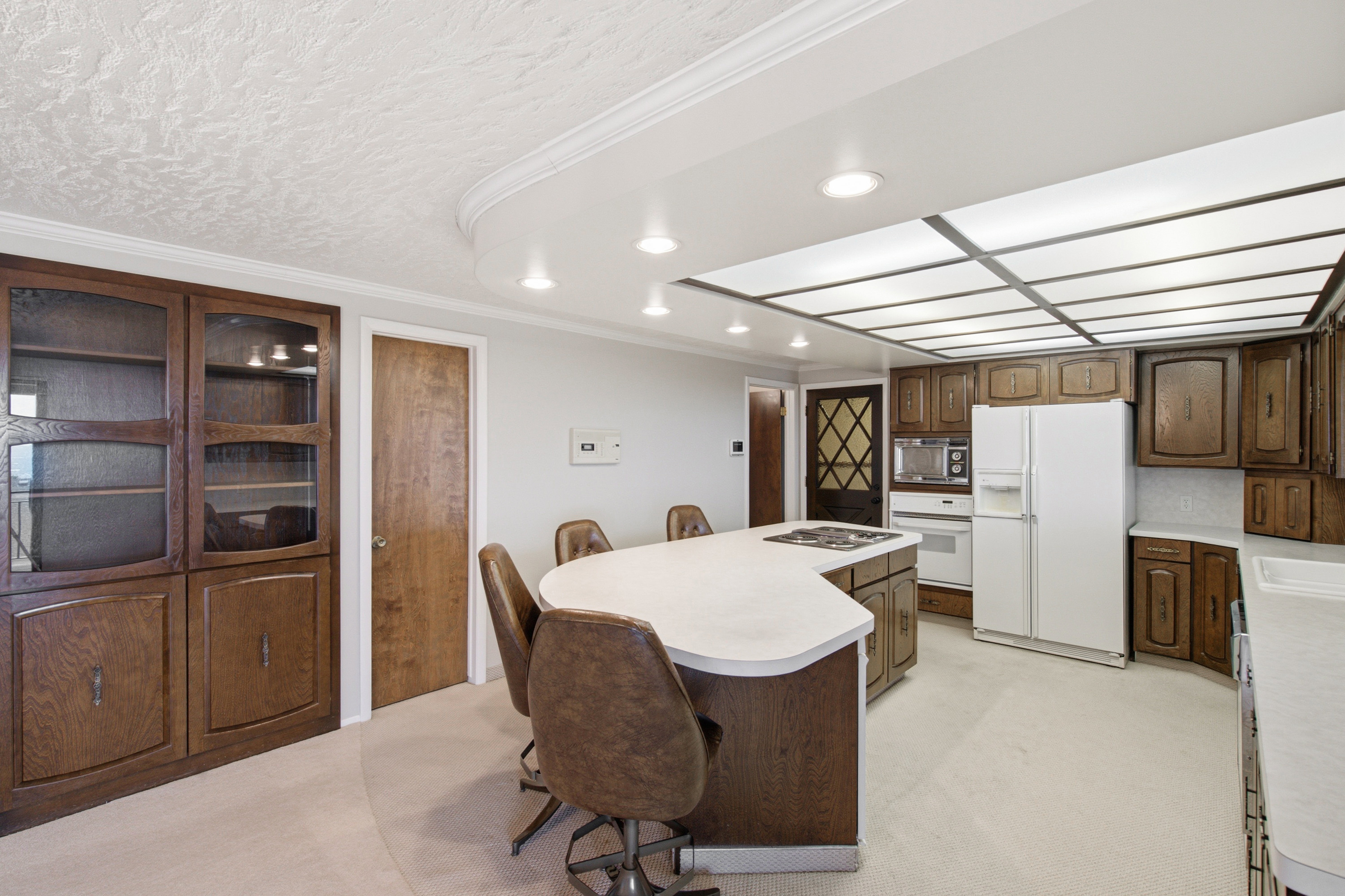 Kitchen featuring wood-finish cabinetry, a large U-shaped island with a cooktop, and an integrated white sink
