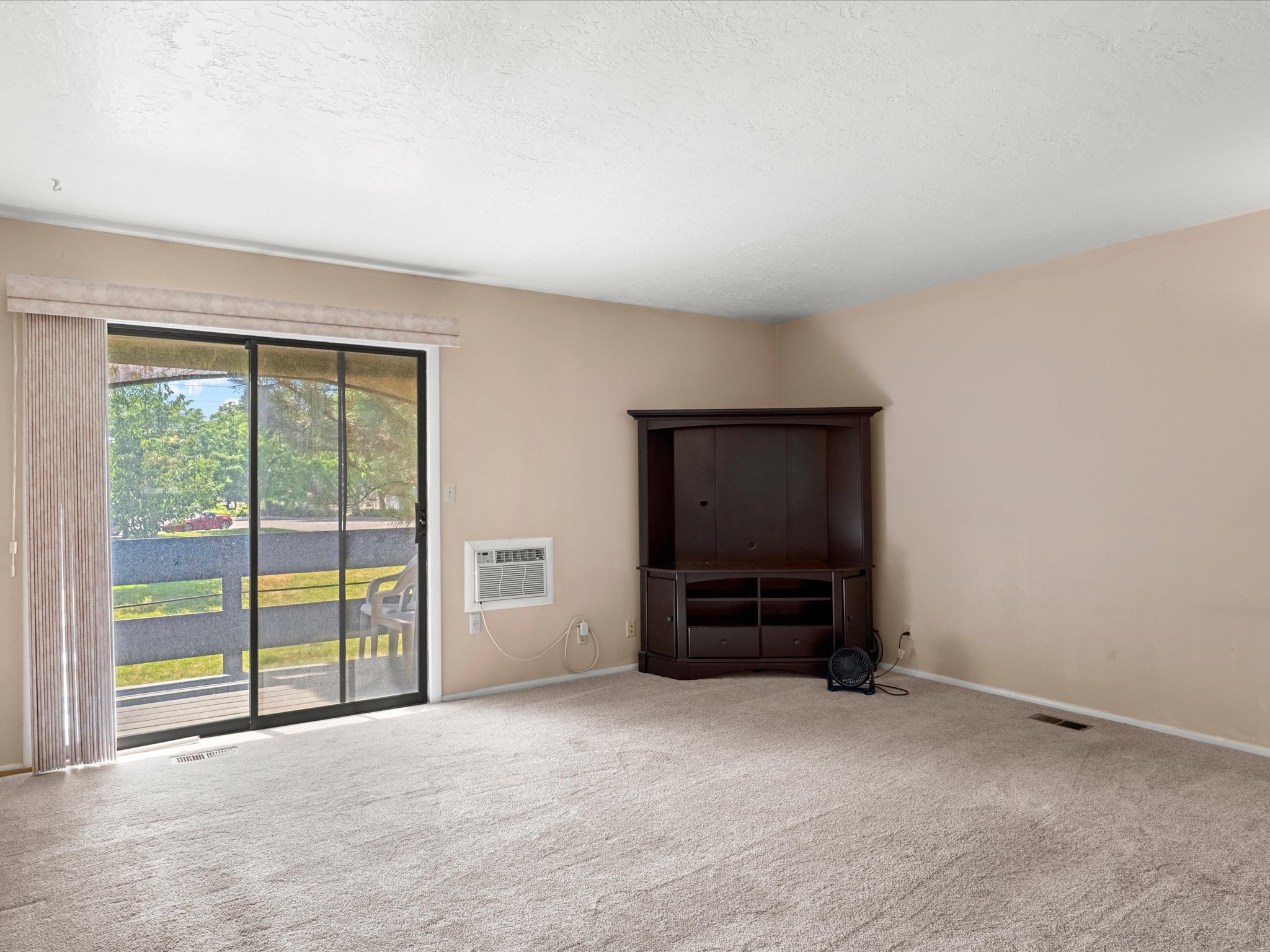 Carpeted living area featuring a large sliding glass door, a window-mounted air conditioning unit, and neutral-toned walls