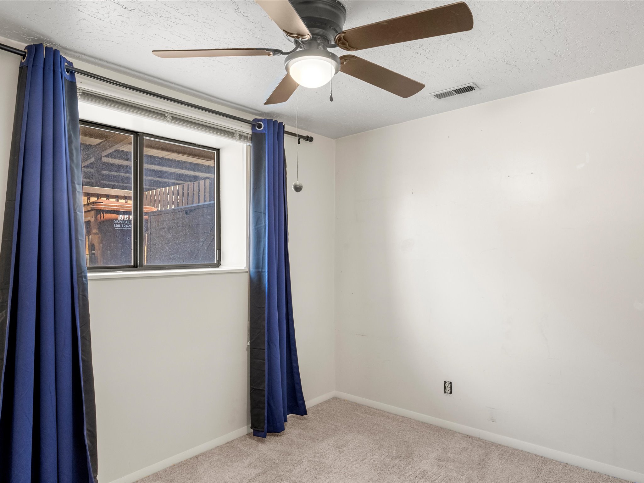 Neutral wall color with textured ceiling, ceiling fan with light fixture, window, and carpeted flooring