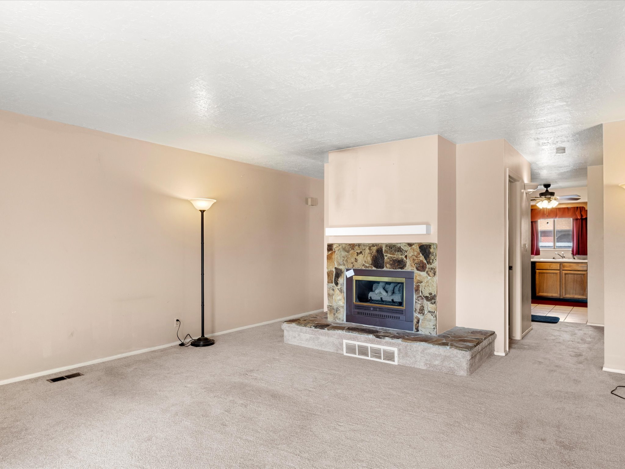 Living area featuring a stone-clad fireplace with a raised hearth, light-toned carpeting, and neutral wall paint