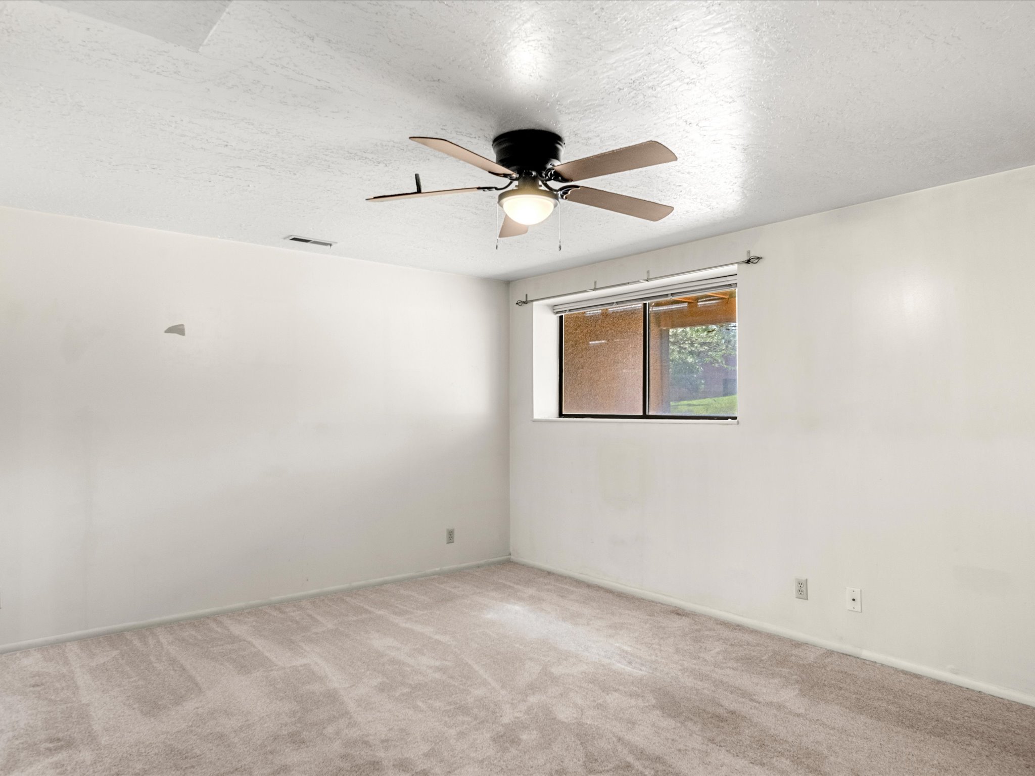 Carpeted room featuring a ceiling fan with integrated lighting, a single window, and textured walls
