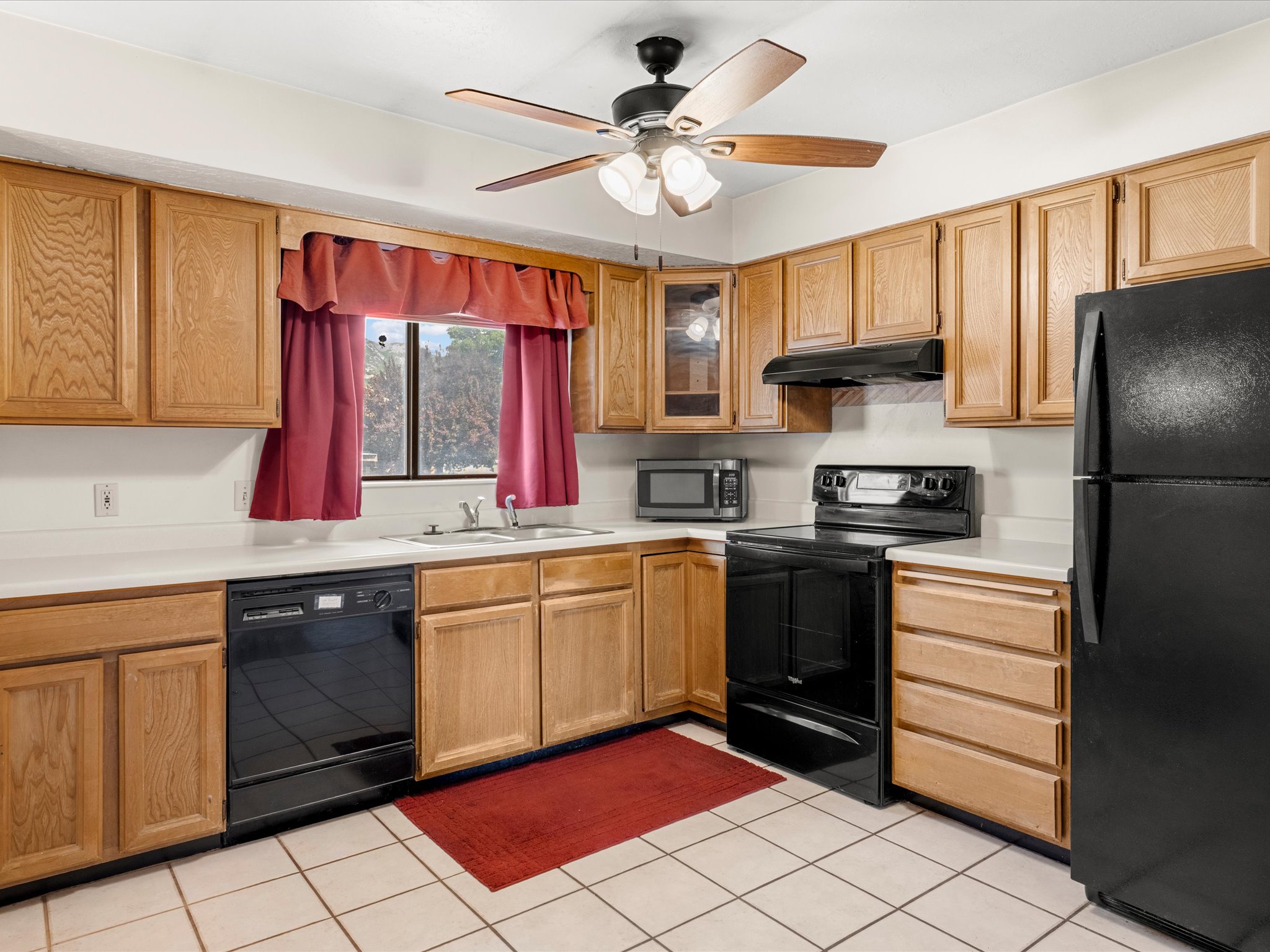 Kitchen featuring wood cabinetry, white countertops, tile flooring, and black appliances including a refrigerator, range, and dishwasher