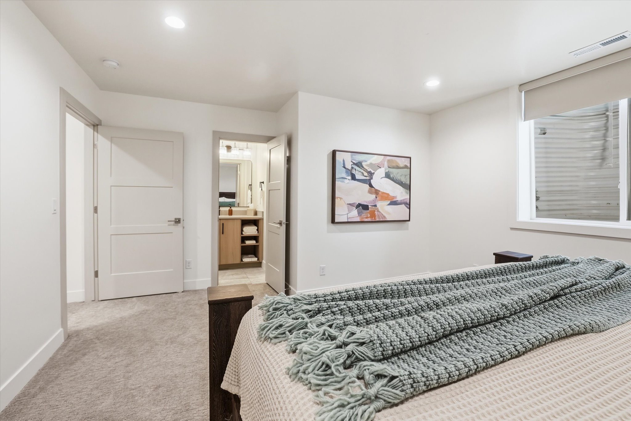 Carpeted bedroom featuring white walls, recessed lighting, and a window with a roller shade