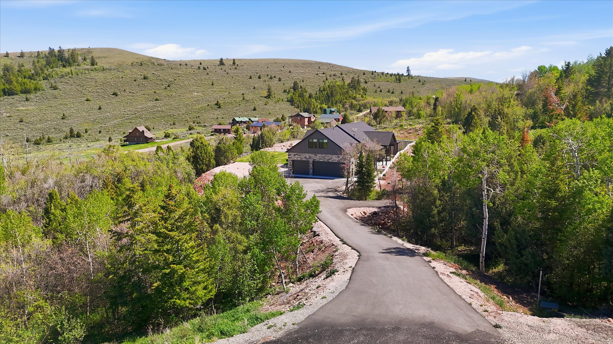 Modern mountain home featuring a dark gray roof, stone facade, and attached three-car garage