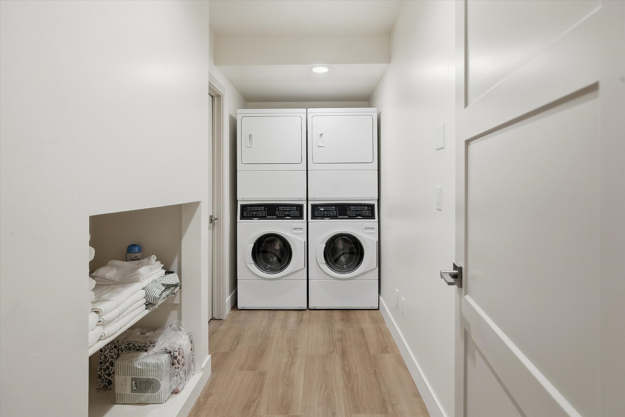 Dedicated laundry area featuring dual stacked washer and dryer units, wood-finish flooring, and recessed lighting
