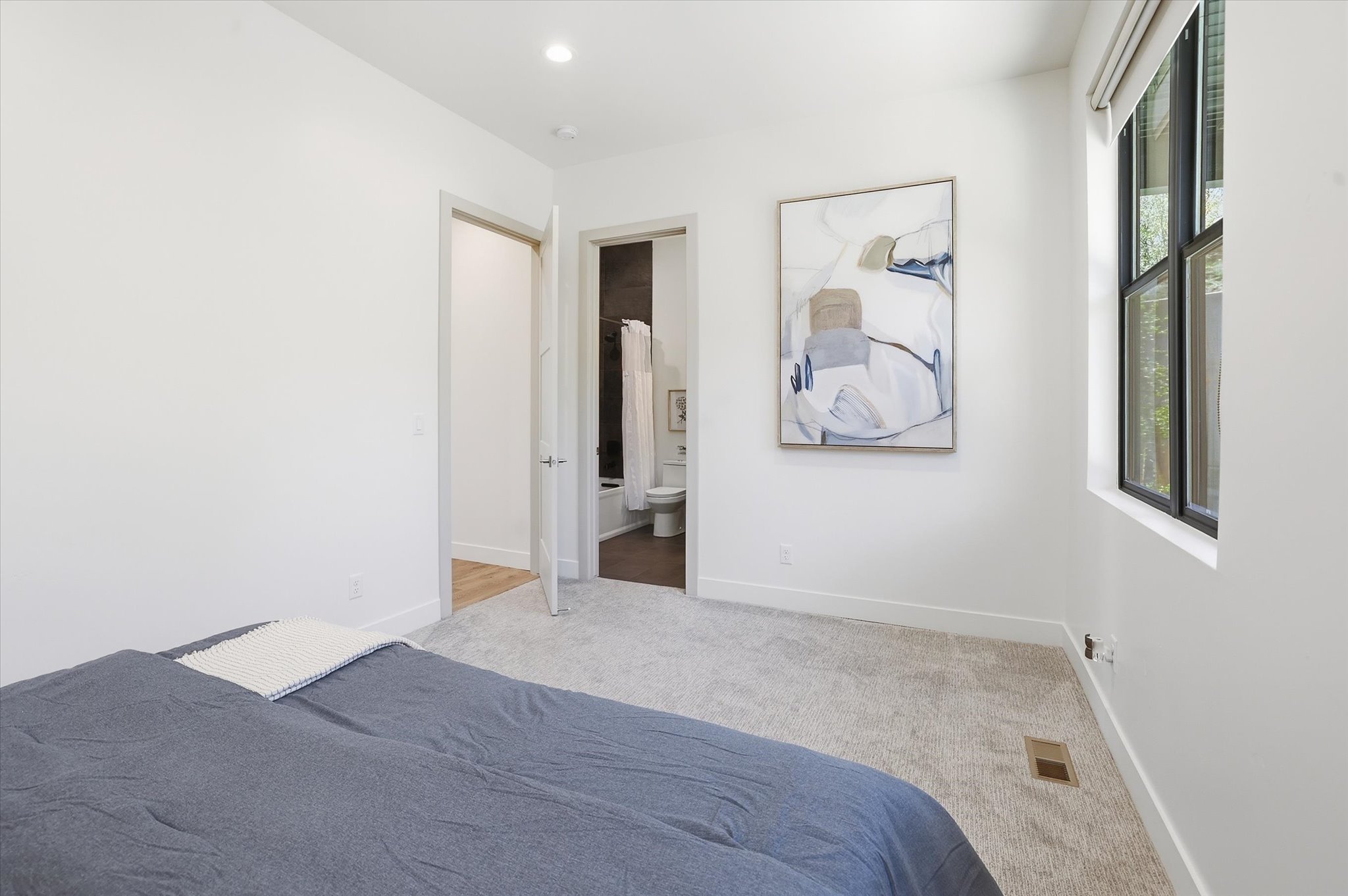 Carpeted bedroom featuring a large window with dark trim, recessed lighting, and a white baseboard