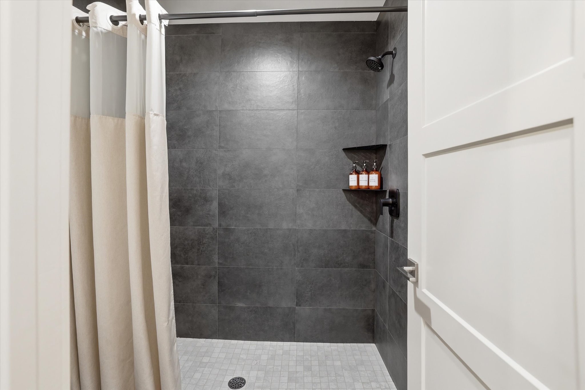 Enclosed shower featuring dark gray large-format wall tiles and a light gray mosaic tile floor