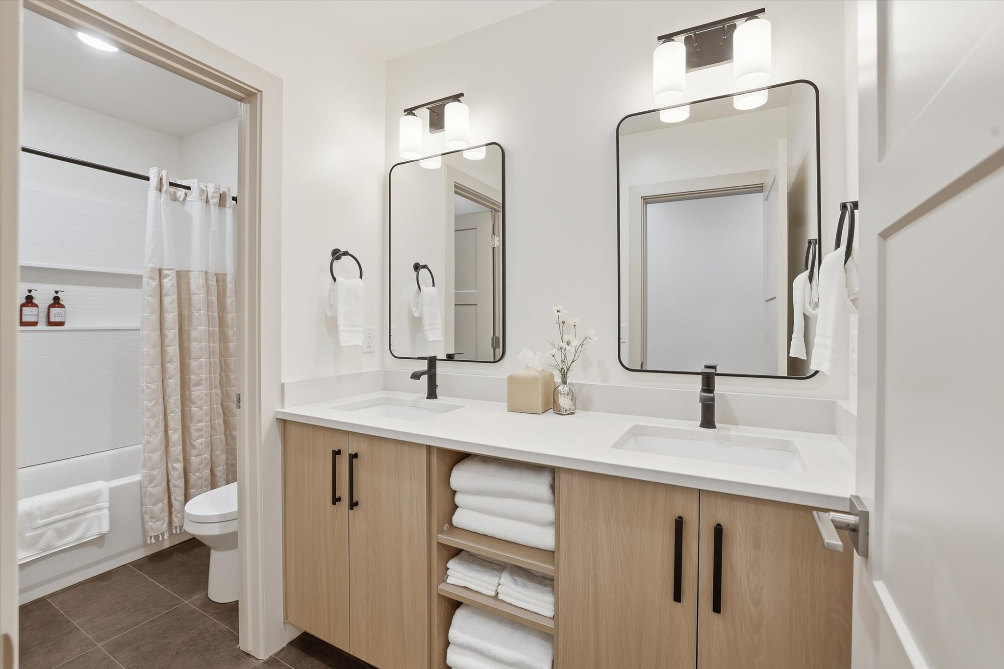 Bathroom featuring a dual vanity with light wood-finish cabinetry, white countertops, and black hardware