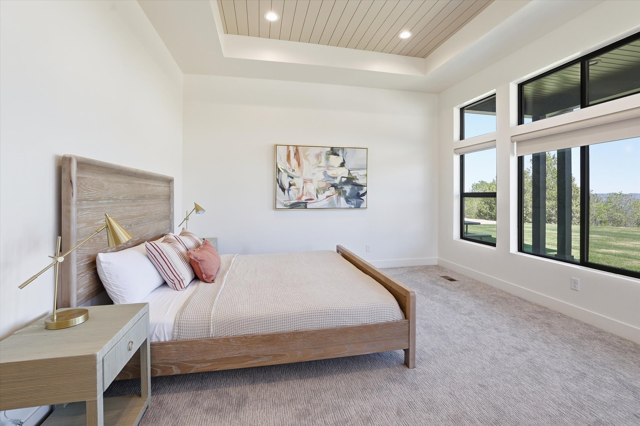 Room featuring an illuminated tray ceiling with wood-finish paneling, expansive windows with roller shades, and light-toned carpeting