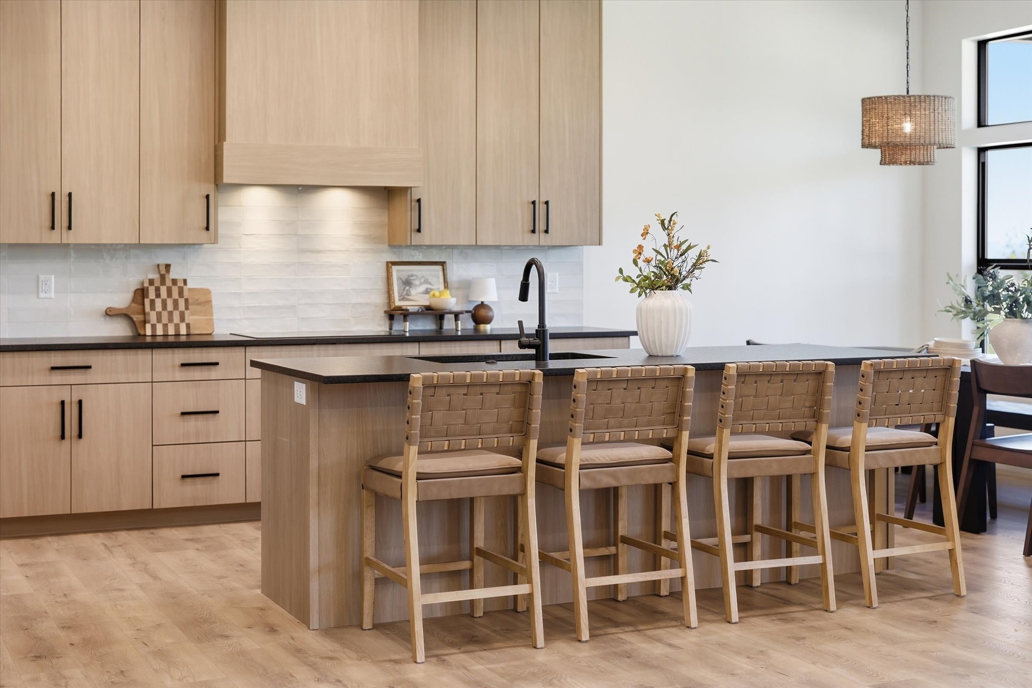 Contemporary kitchen featuring light wood-finish cabinetry, a central island with bar seating, dark countertops, and a subway tile backsplash