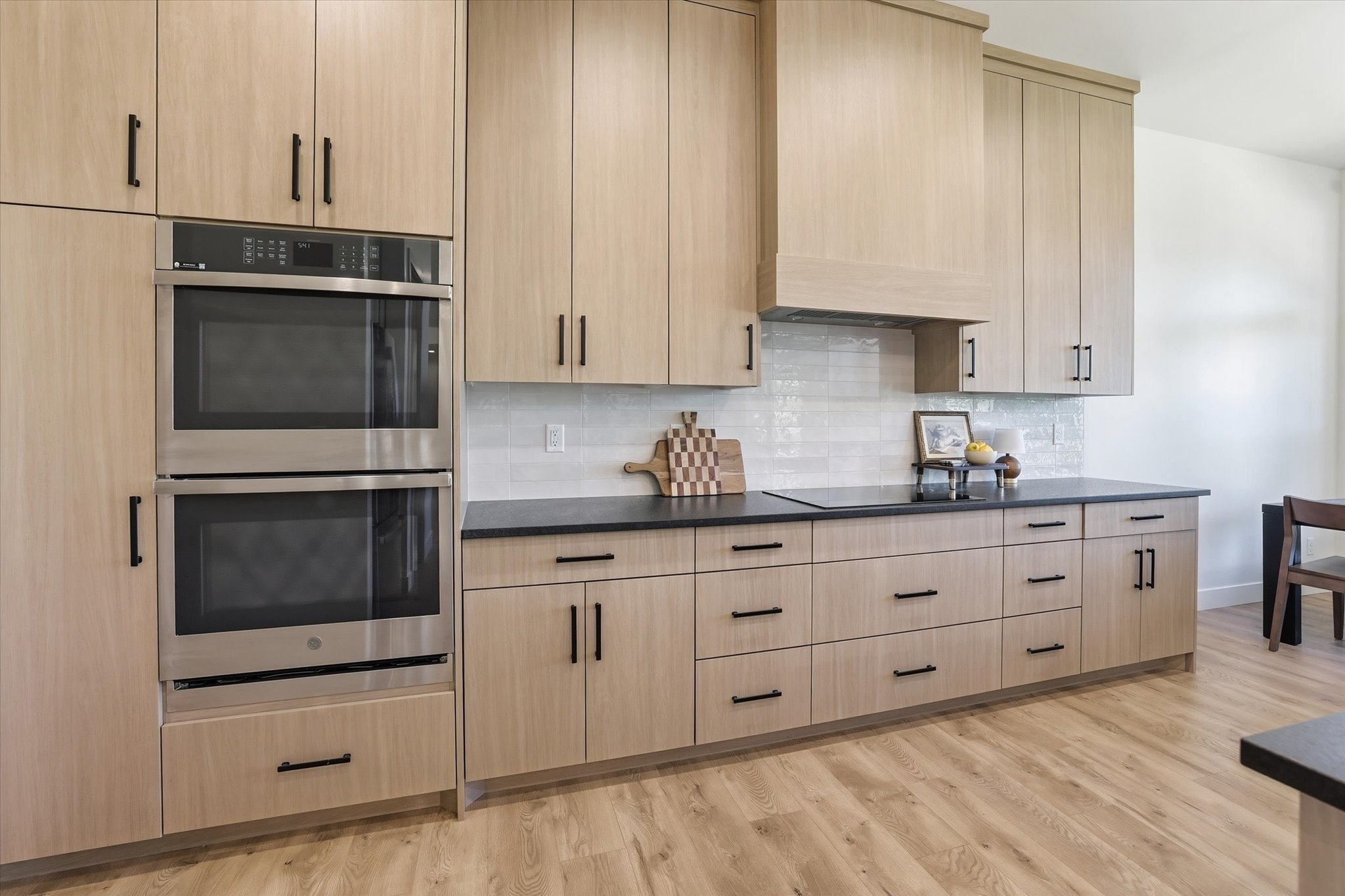 Kitchen featuring light wood-finish cabinetry with black hardware, black countertops, and a white subway tile backsplash