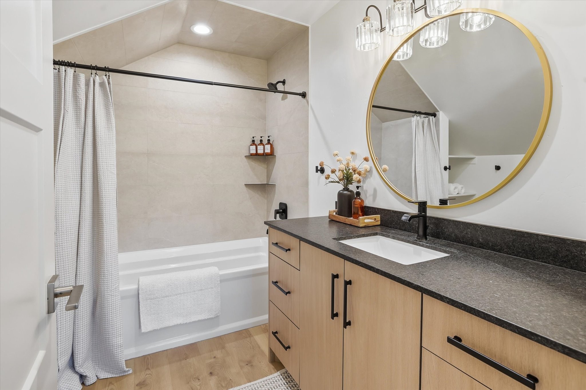 Bathroom featuring a light wood-finish vanity with black hardware, a dark countertop, and an undermount sink