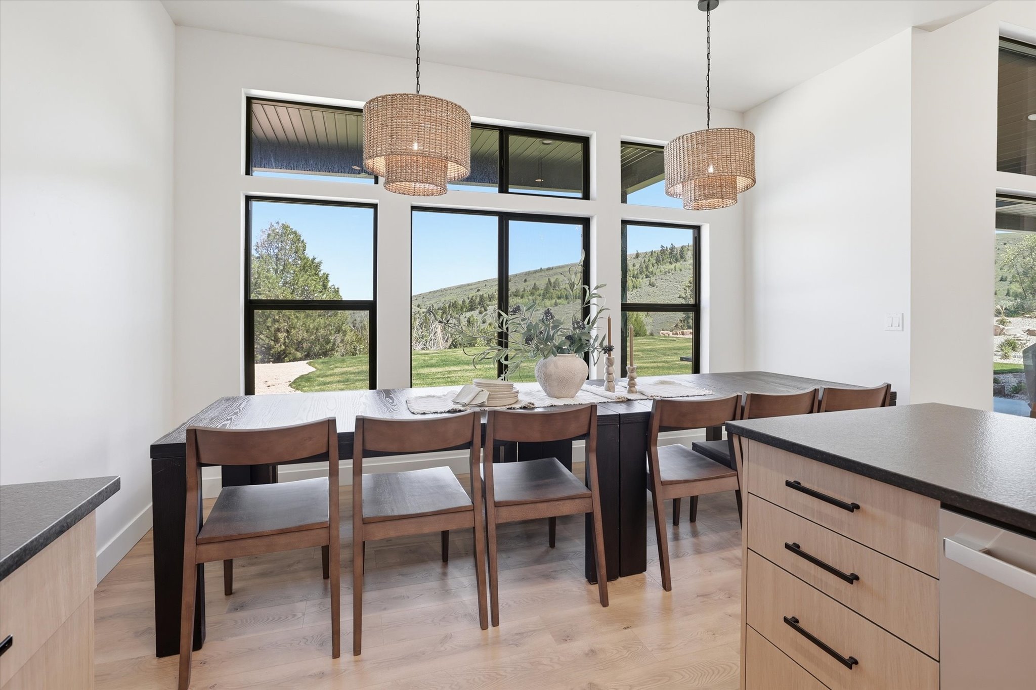 Dining area featuring multiple windows, two woven pendant lights, light wood-finish flooring, and a built-in kitchen island with light wood-finish cabinetry