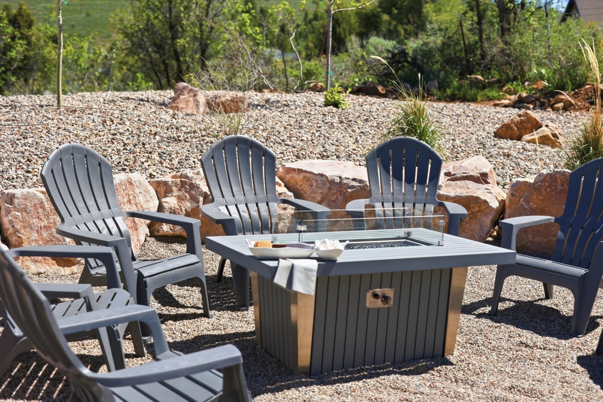 Outdoor gathering area featuring a central fire pit with a glass enclosure, surrounded by Adirondack-style chairs