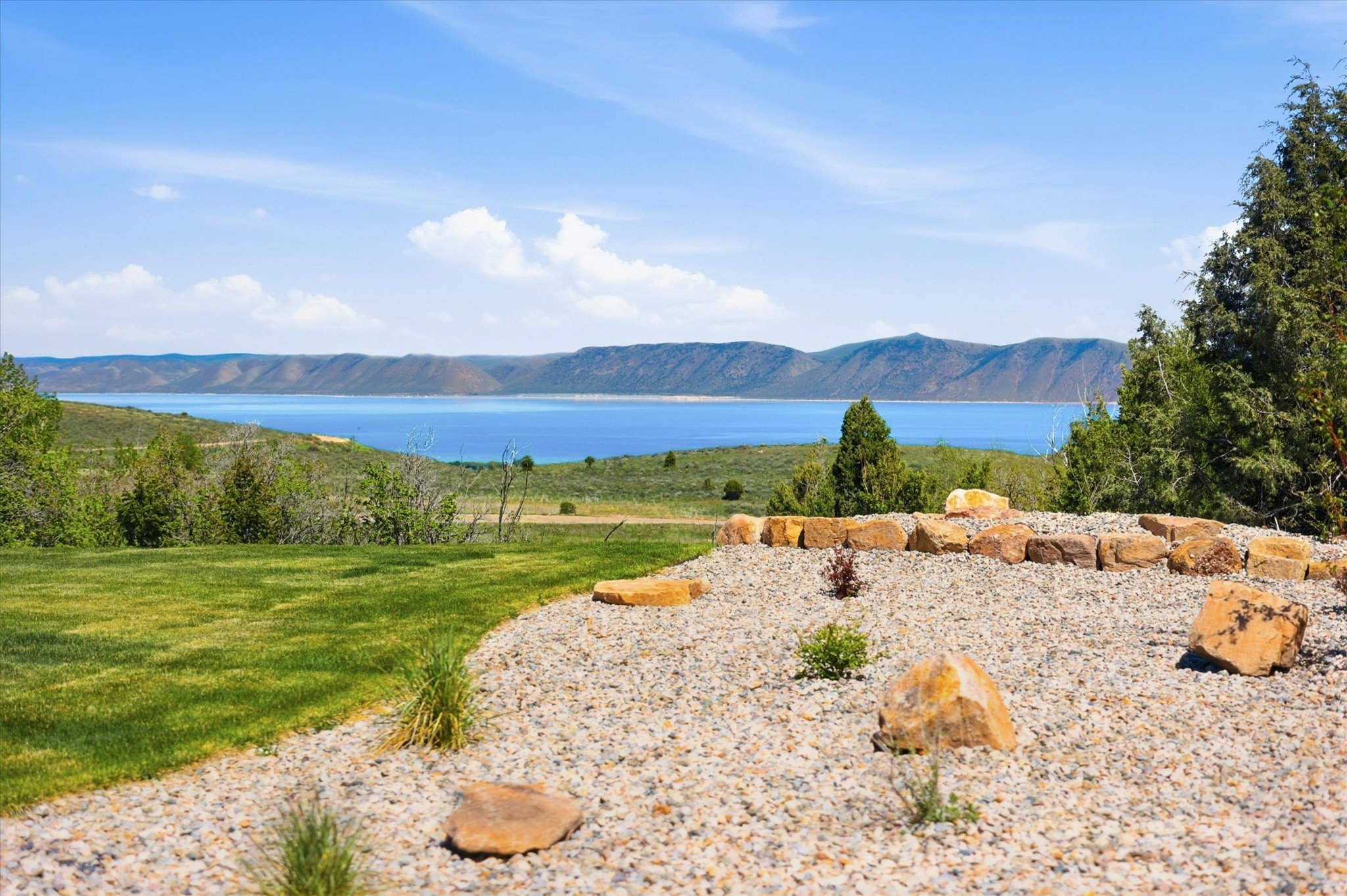 Expansive outdoor space featuring a broad lawn, a decorative rock garden with natural stone accents, and mature evergreen plantings