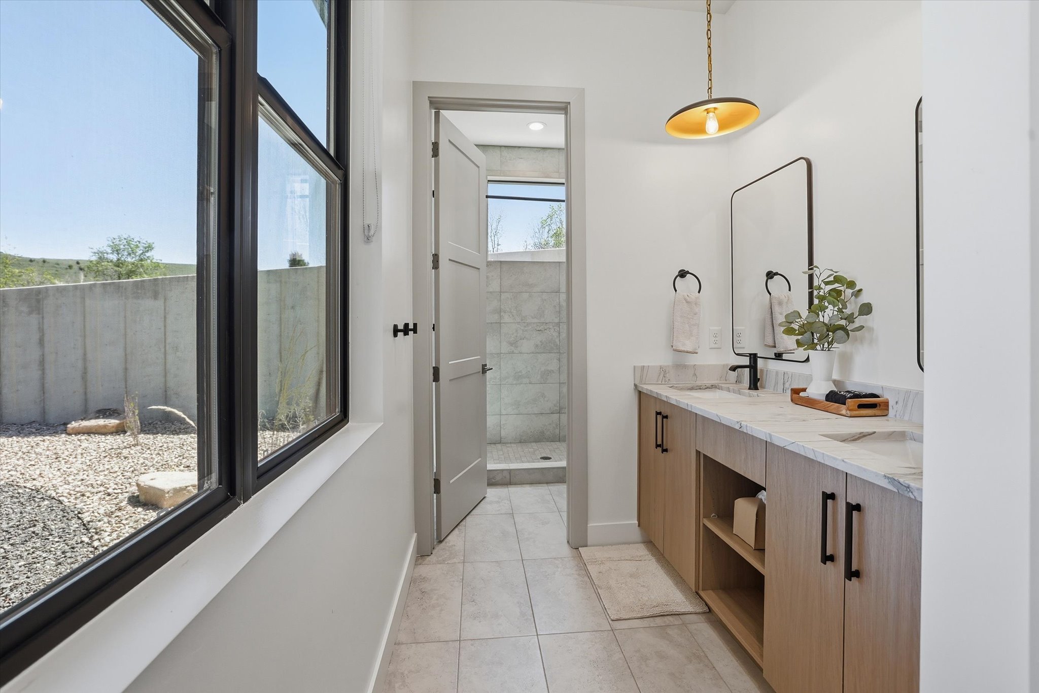 Modern bathroom featuring a dual vanity with light wood-finish cabinetry, stone countertops, and matte black fixtures