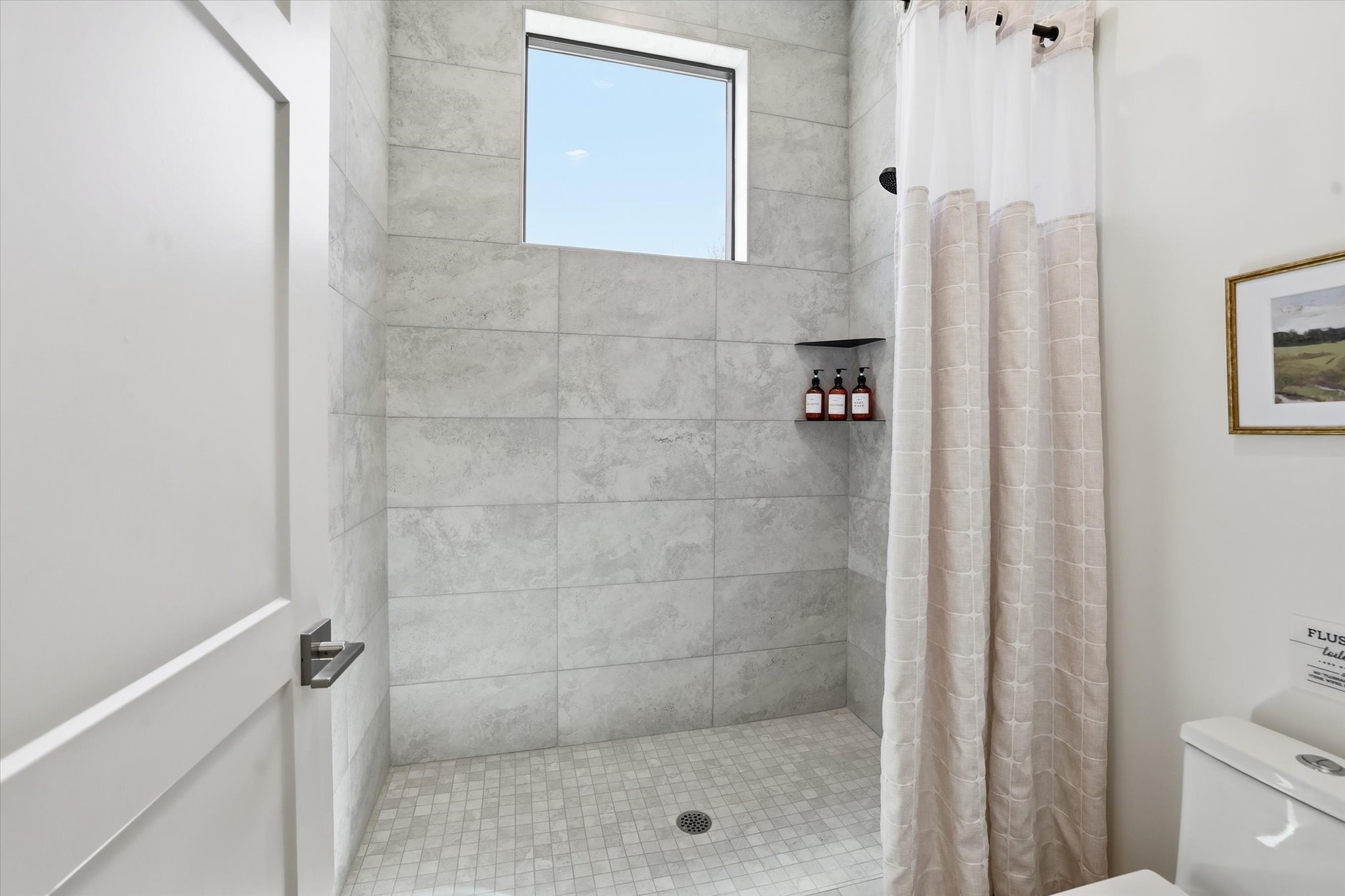 Walk-in shower featuring large format gray wall tiling and mosaic floor tiles