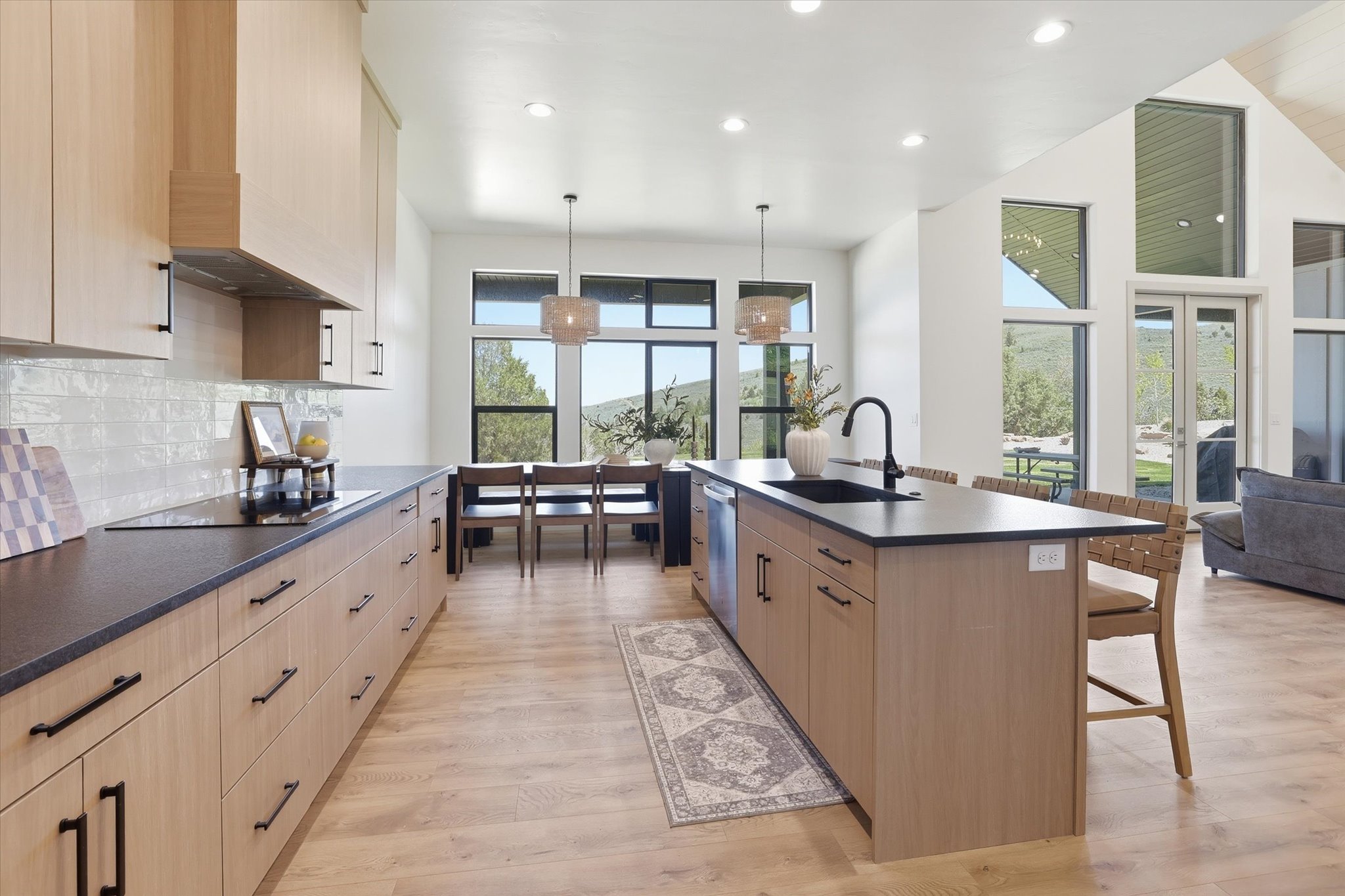 Modern kitchen featuring wood-finish cabinetry, dark countertops, a large center island with an undermount sink, and light wood-finish flooring
