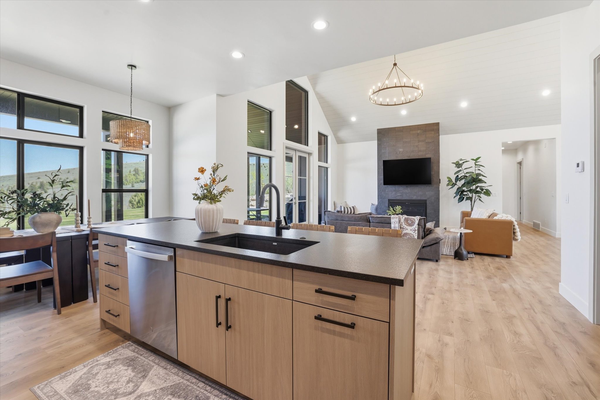 Kitchen island with a dark countertop and undermount sink, integrated stainless steel dishwasher, light wood-finish cabinetry, and black hardware