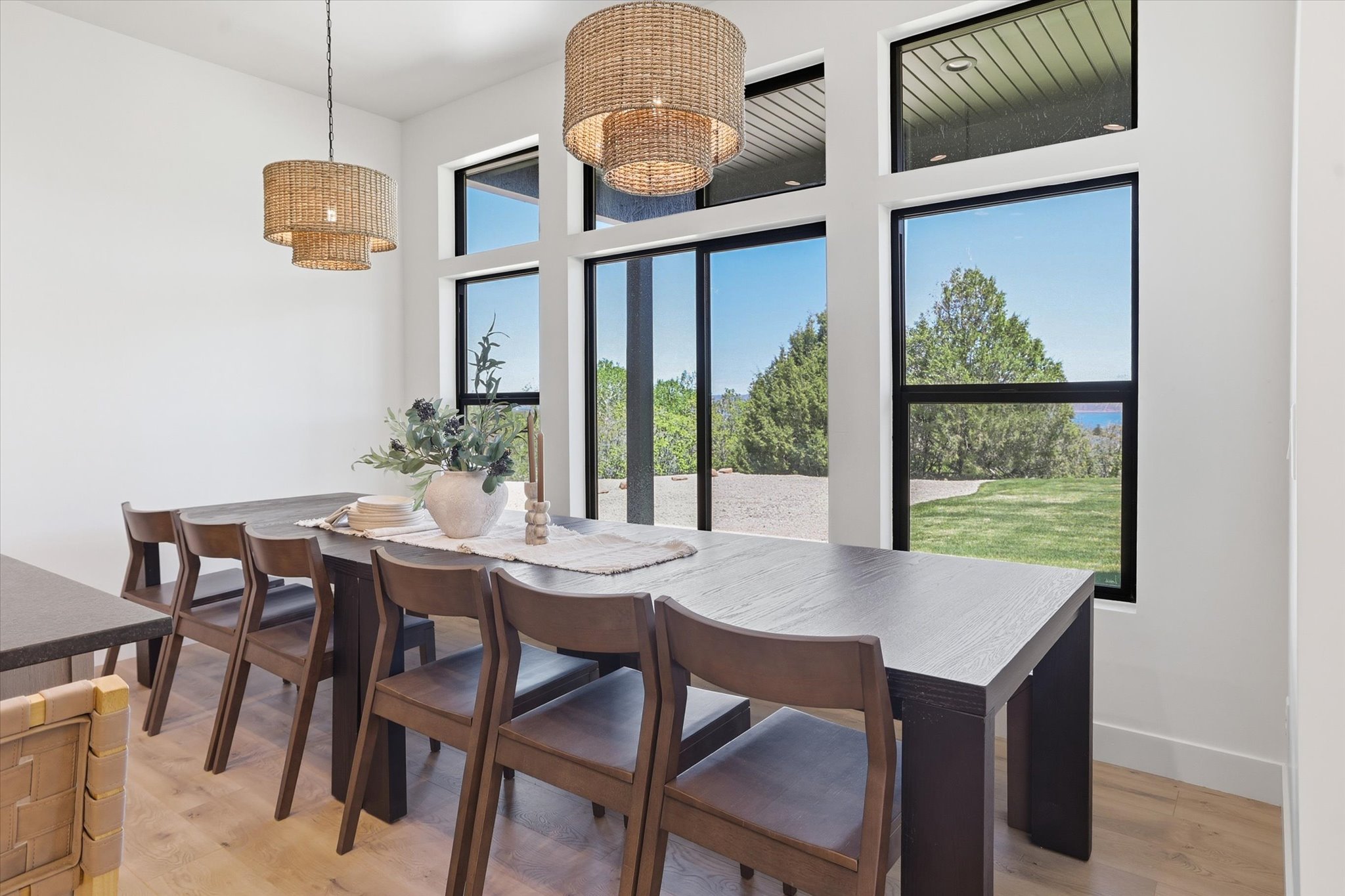 Dining area featuring a wall of floor-to-ceiling windows, light wood-finish flooring, and two woven pendant light fixtures